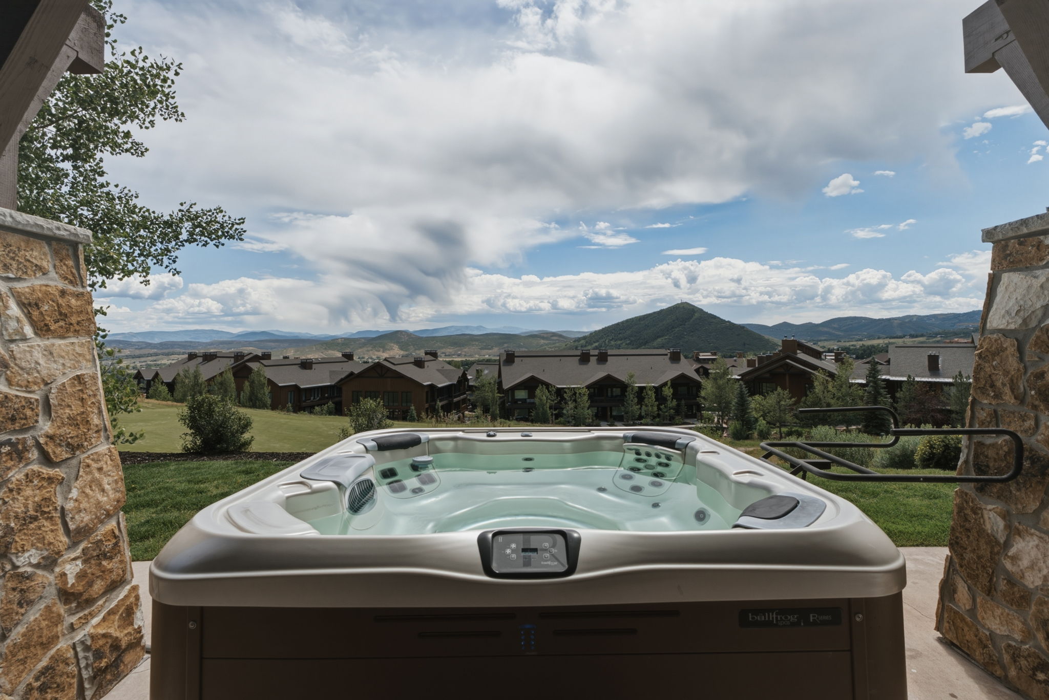 Outdoor hot tub featuring a stone-clad columns, golf course views, and mountain scenery