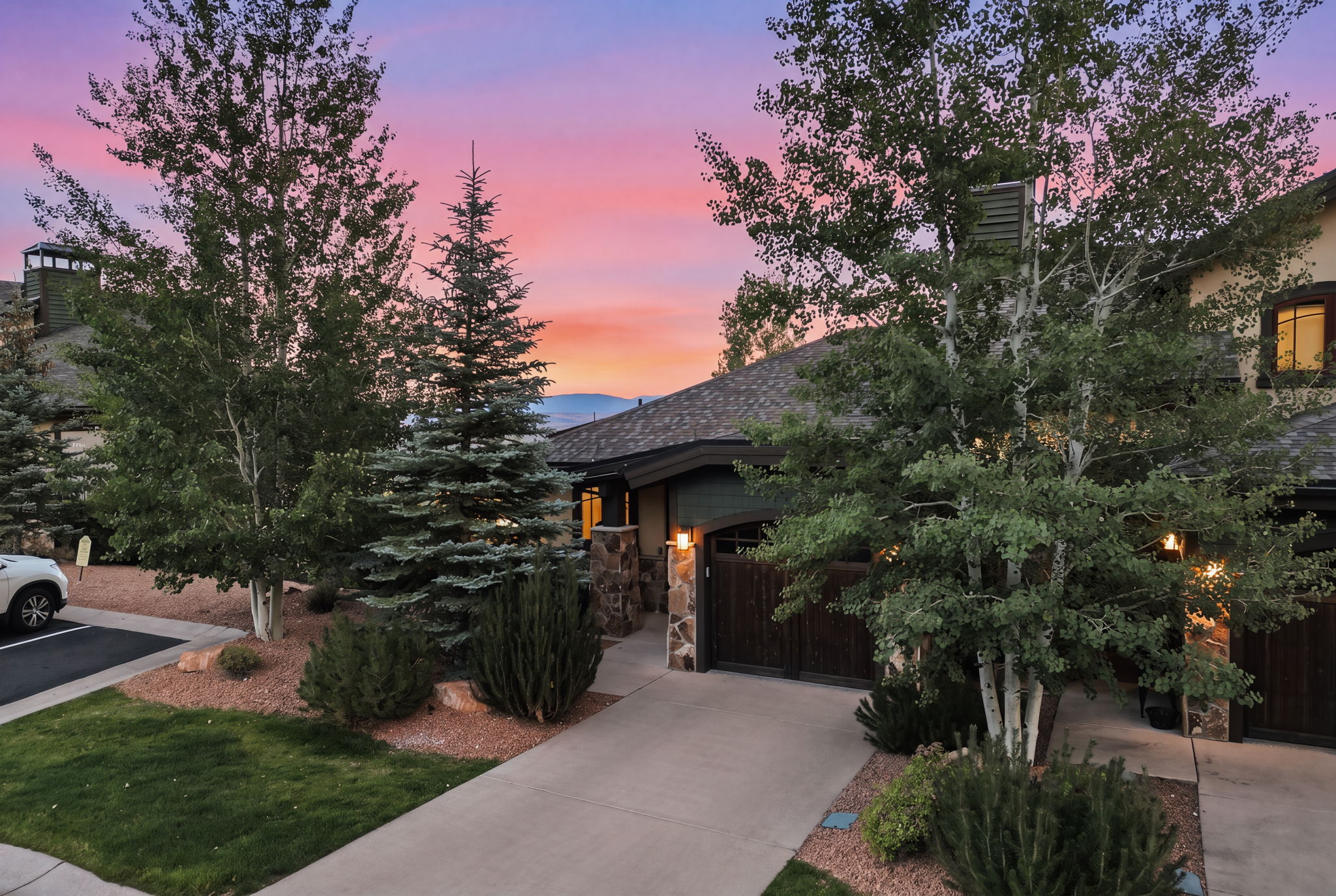 Twilight views of the front door, concrete driveway, craftsman-style stone accents exterior featuring a dark wood garage door, and asphalt shingle roofing.