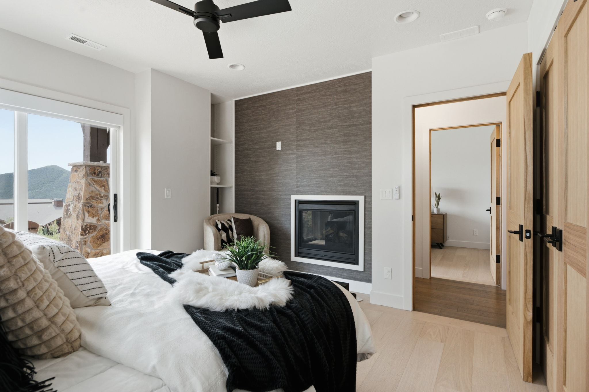 Bedroom featuring a modern linear fireplace, textured accent wall, and light wood-finish flooring