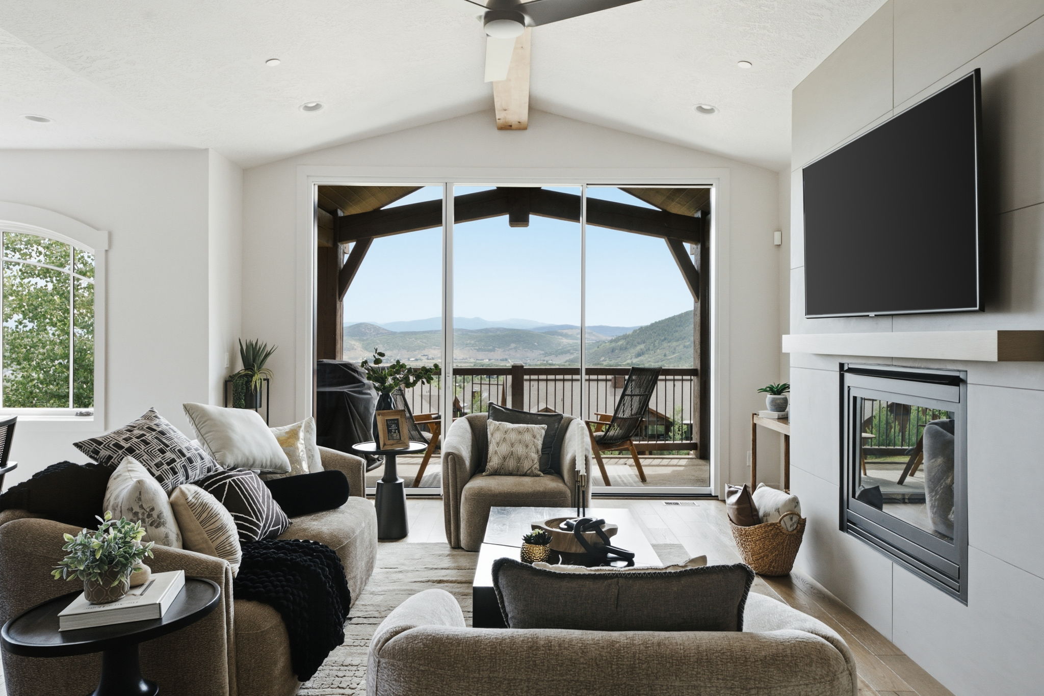 Spacious living area featuring expansive glass sliding doors, a built-in fireplace with a hearth, vaulted ceilings with a wood beam, and wood-finish flooring