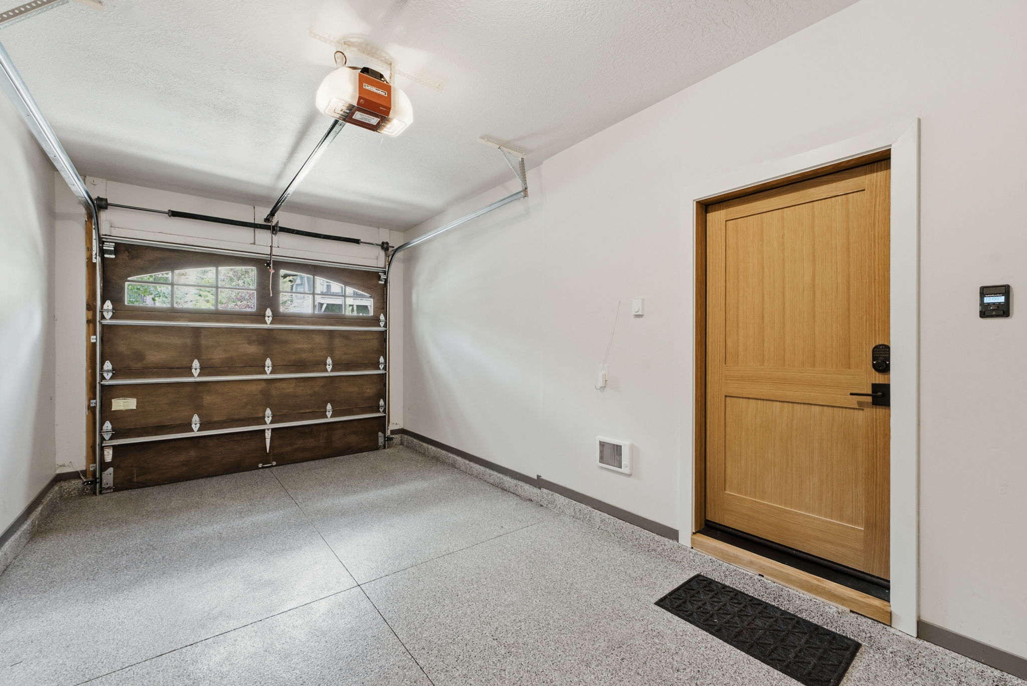 Single-car garage featuring a wood-finish overhead door with arched window panels, a light wood-finish interior door with black hardware, and a speckled epoxy floor coating