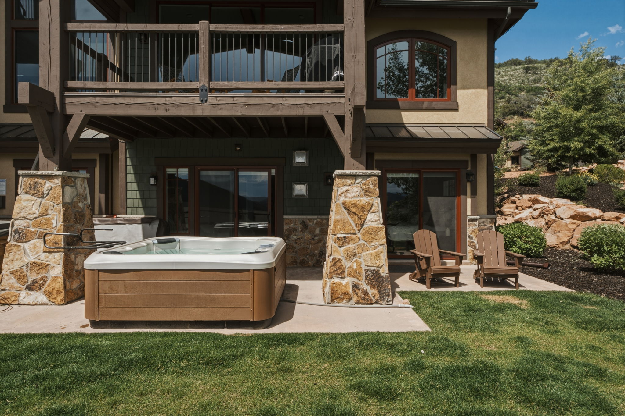 Lower-level patio featuring a built-in hot tub, concrete hardscaping, and stone-clad columns