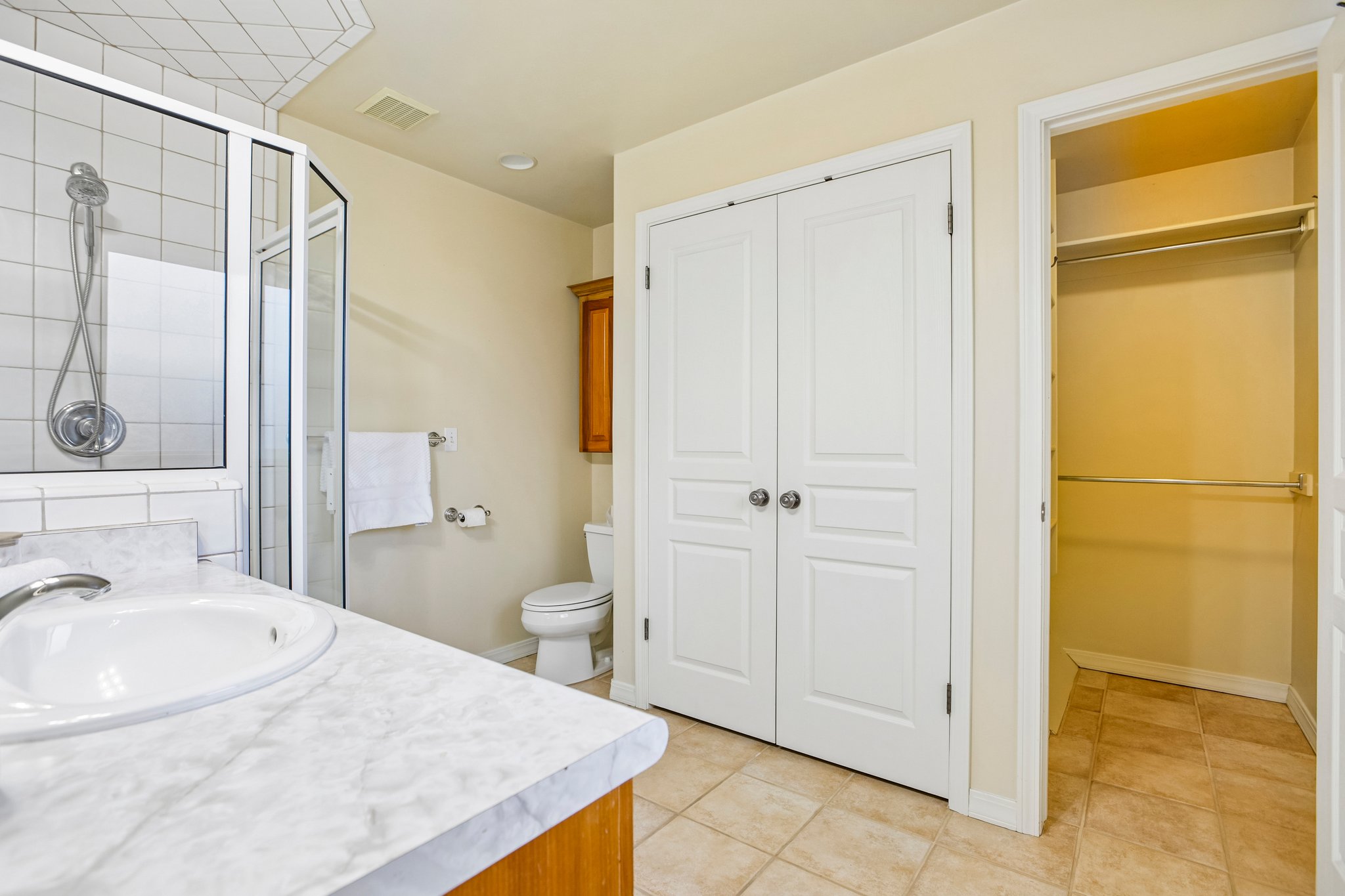 Bathroom featuring a glass-enclosed shower, single vanity with a white countertop and integrated sink, toilet, and tiled flooring