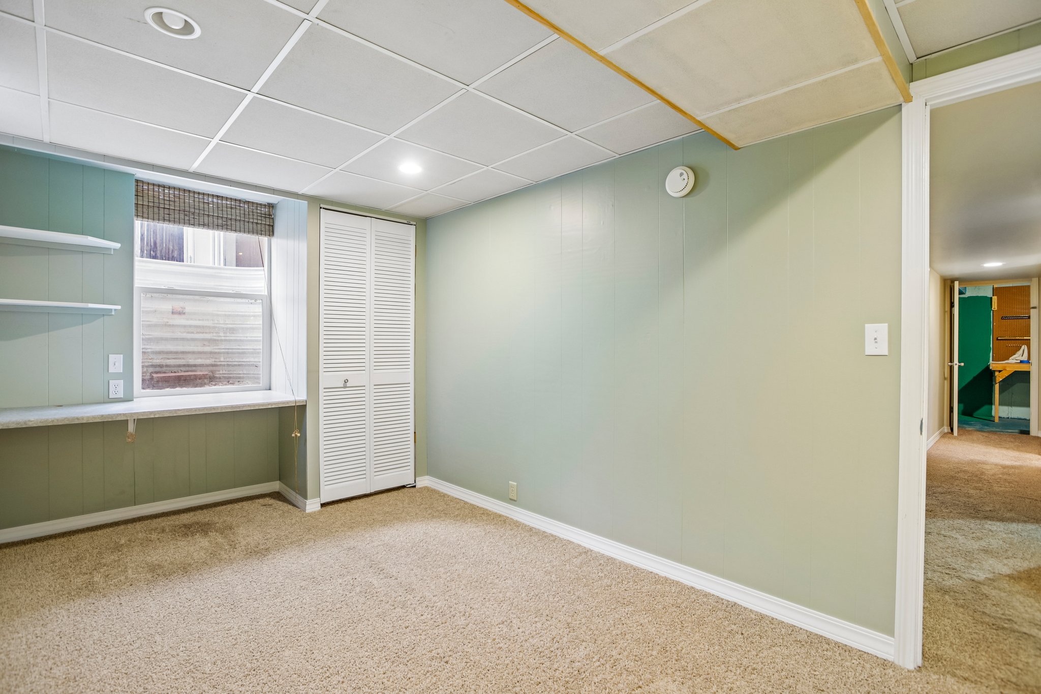 Interior room featuring carpet flooring, drop ceiling with recessed lighting, built-in shelving, and bifold closet doors