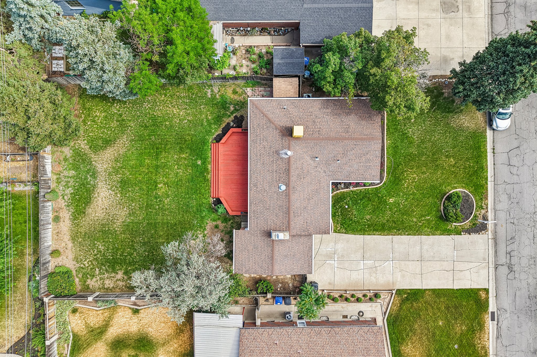 Expansive backyard featuring a red wood-finish deck, mature trees, and a concrete driveway