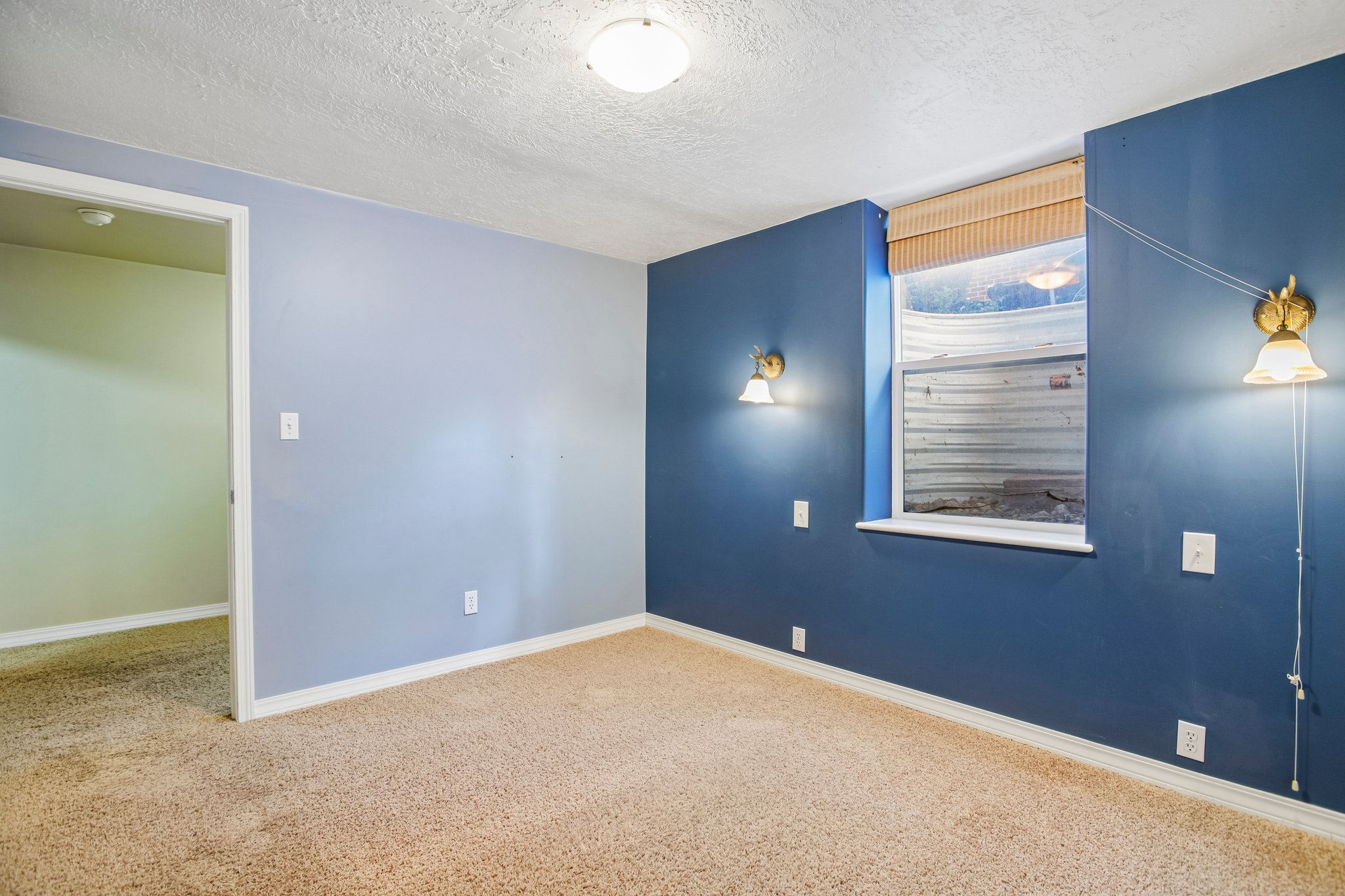 Carpeted room with a window featuring a light-colored blind, two wall-mounted sconces, and a ceiling-mounted light fixture