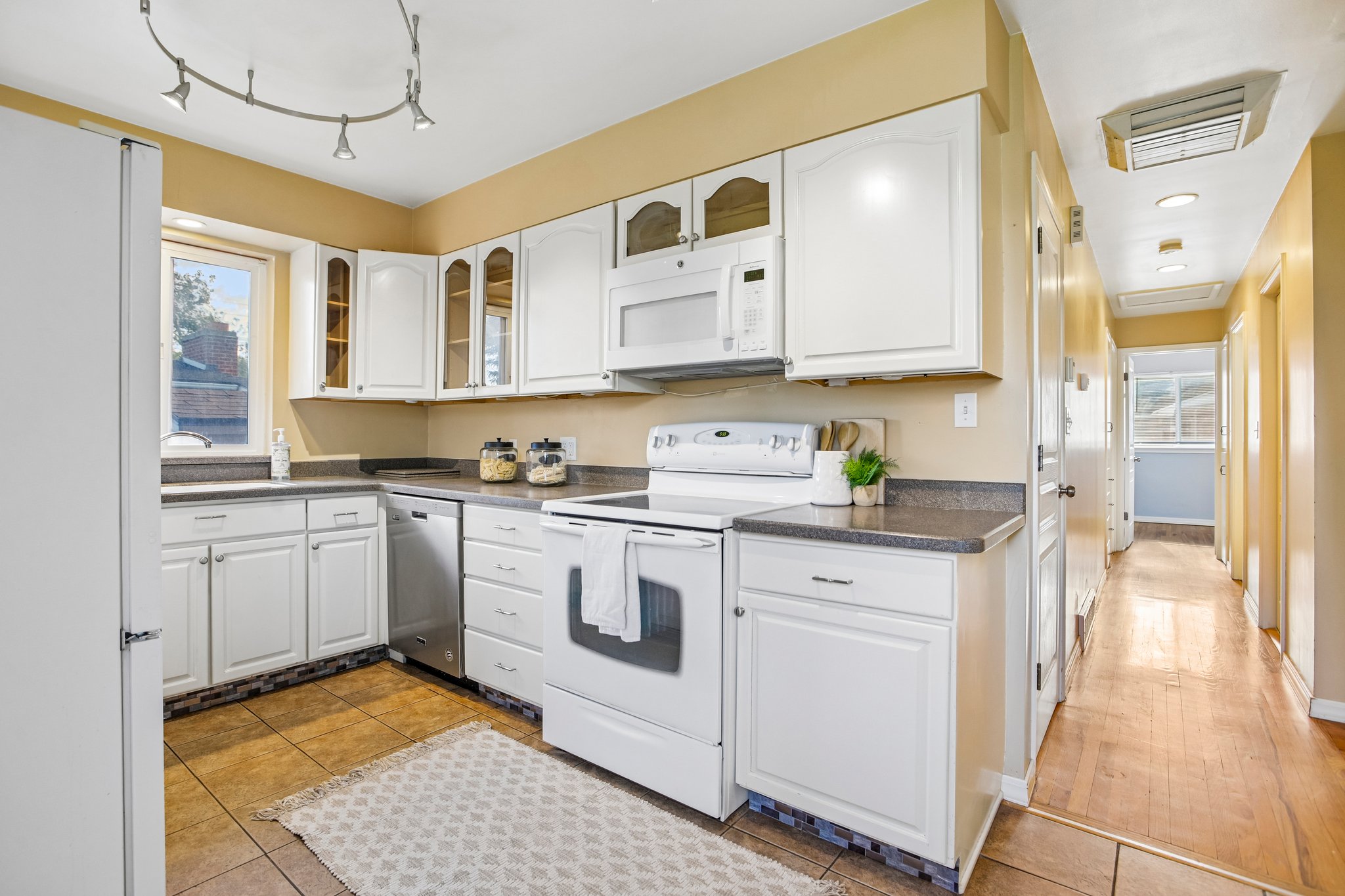 White cabinetry kitchen featuring a window, dark countertops, a white oven, a built-in microwave, and track lighting