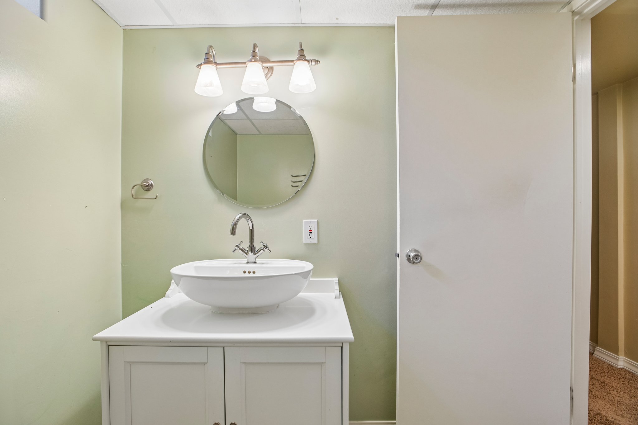 Bathroom vanity featuring a vessel sink, brushed nickel faucet, round mirror, and a three-light vanity fixture
