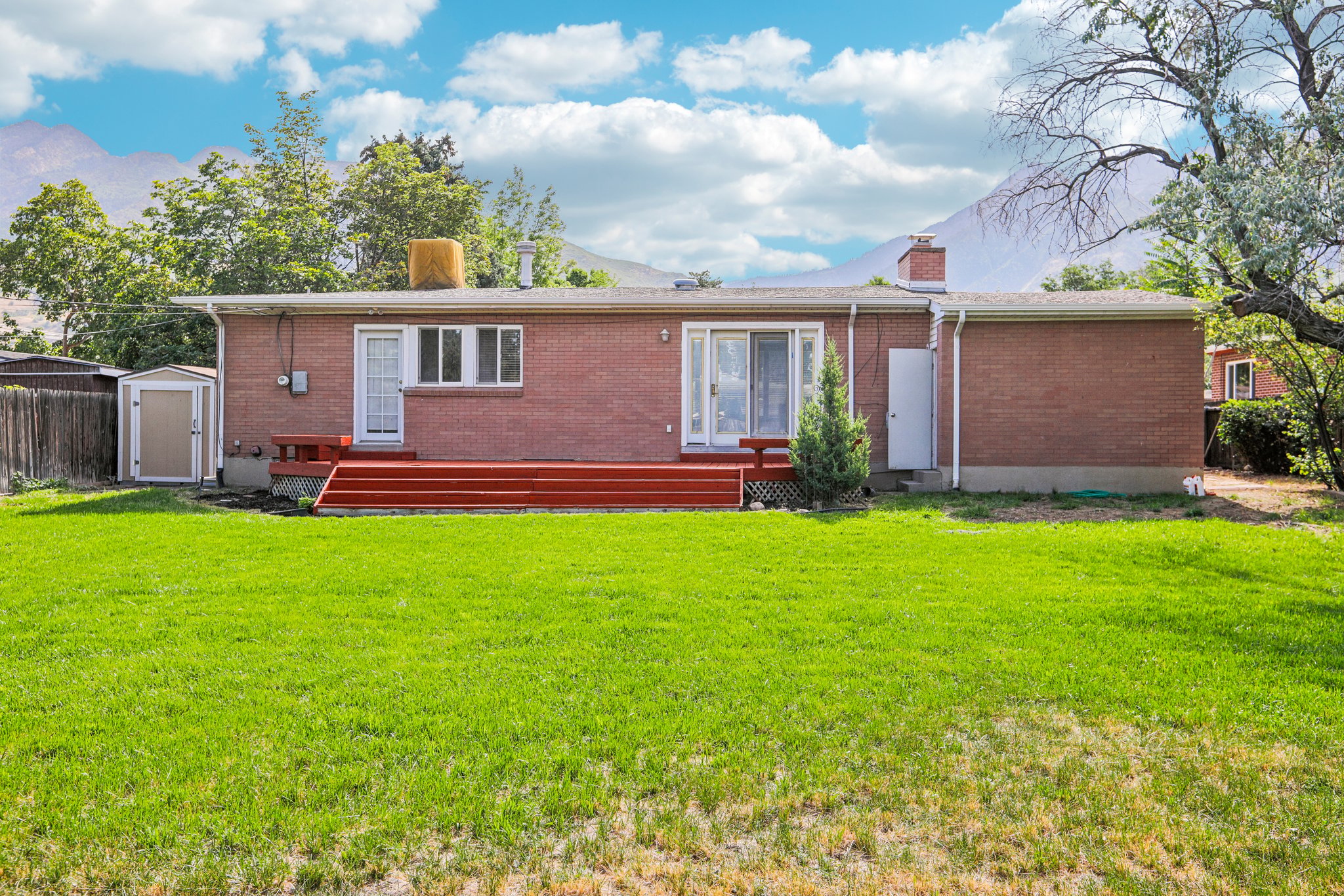 Expansive backyard featuring a manicured lawn, red brick exterior, a red-stained wood deck, and a sliding glass door