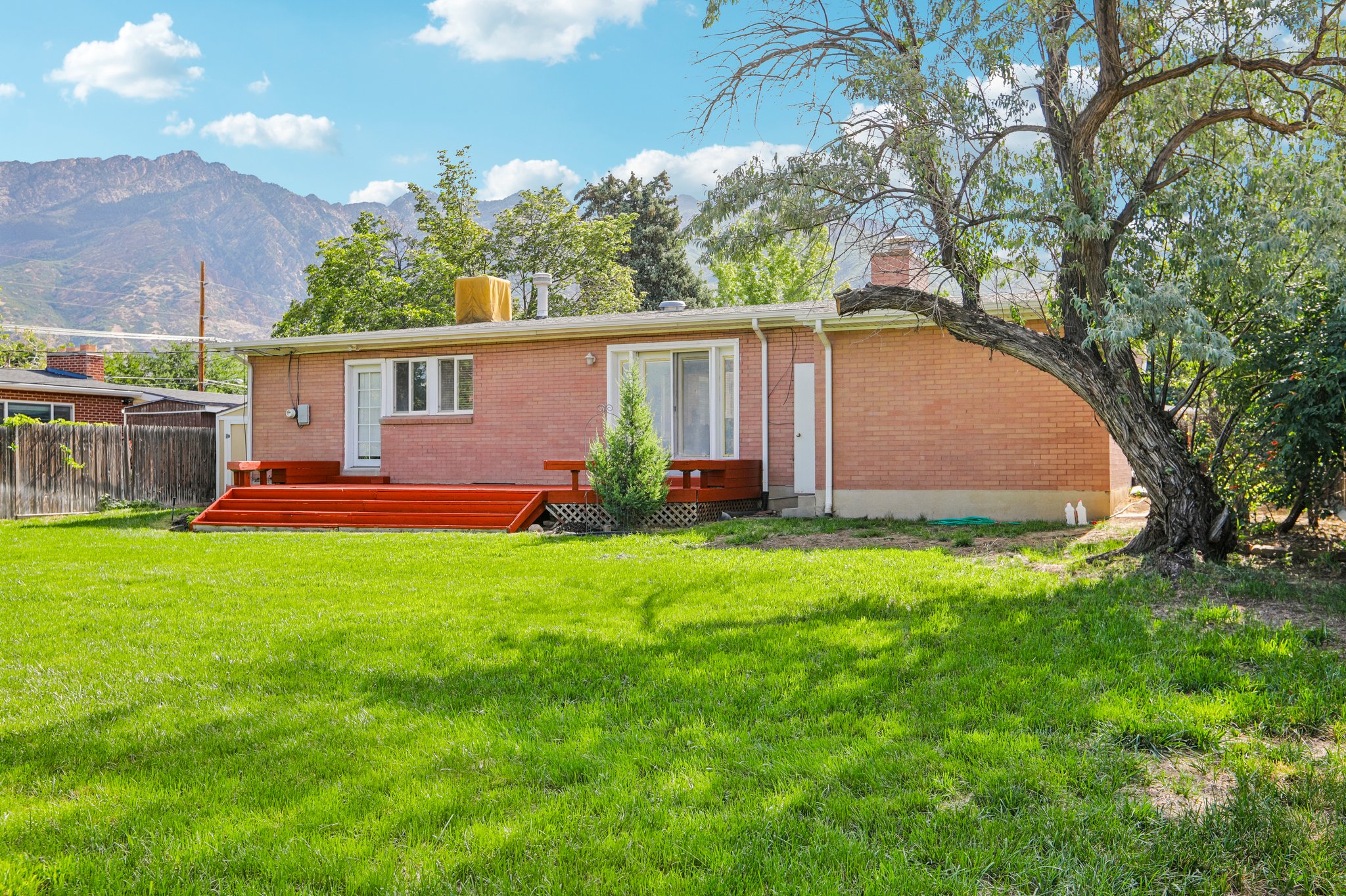 Expansive green lawn with a red-stained wood deck at the rear of the brick-clad home
