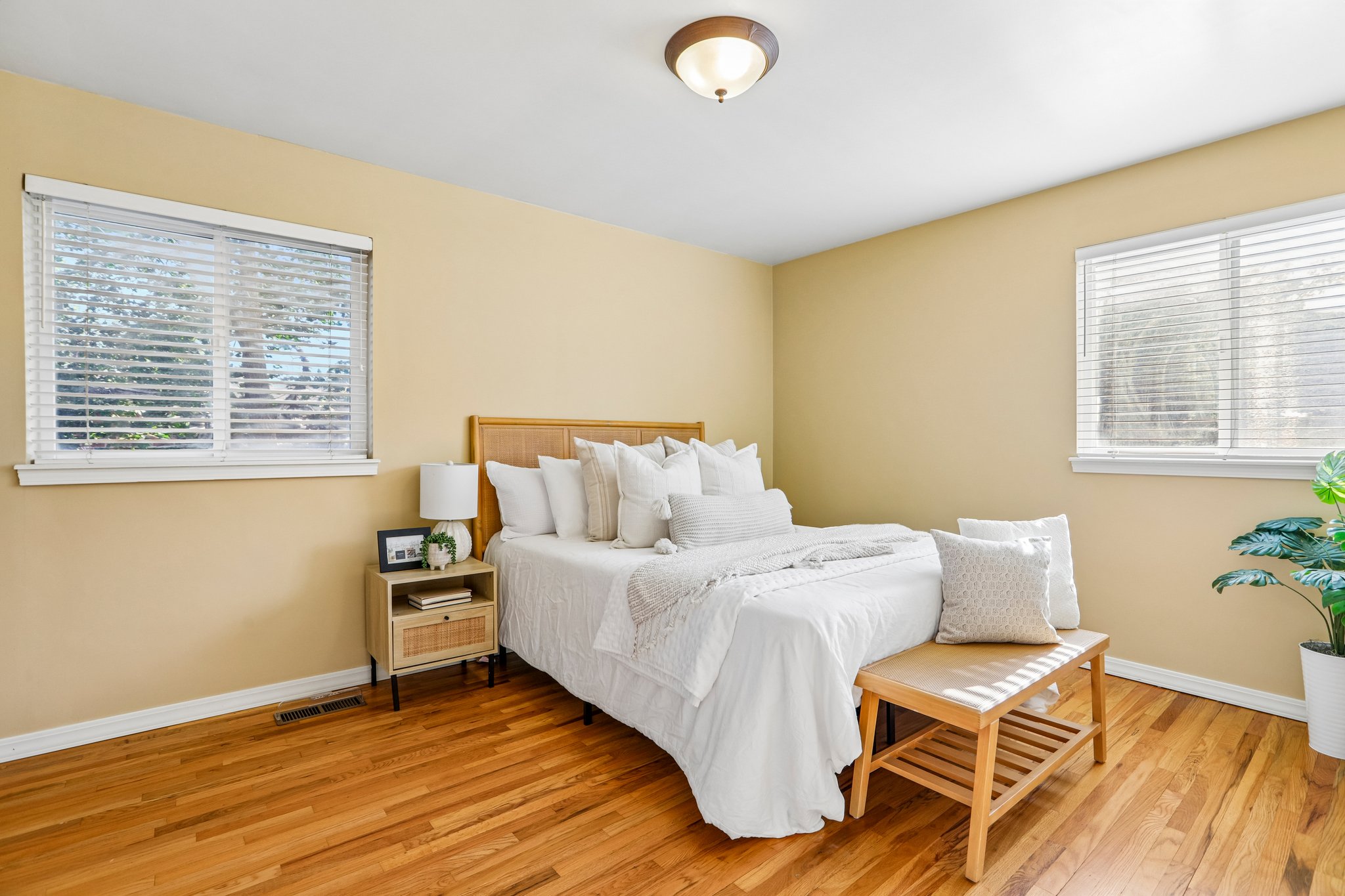 Bedroom featuring wood-finish flooring, two windows with blinds, a ceiling-mounted light fixture, and warm-toned wall finishes