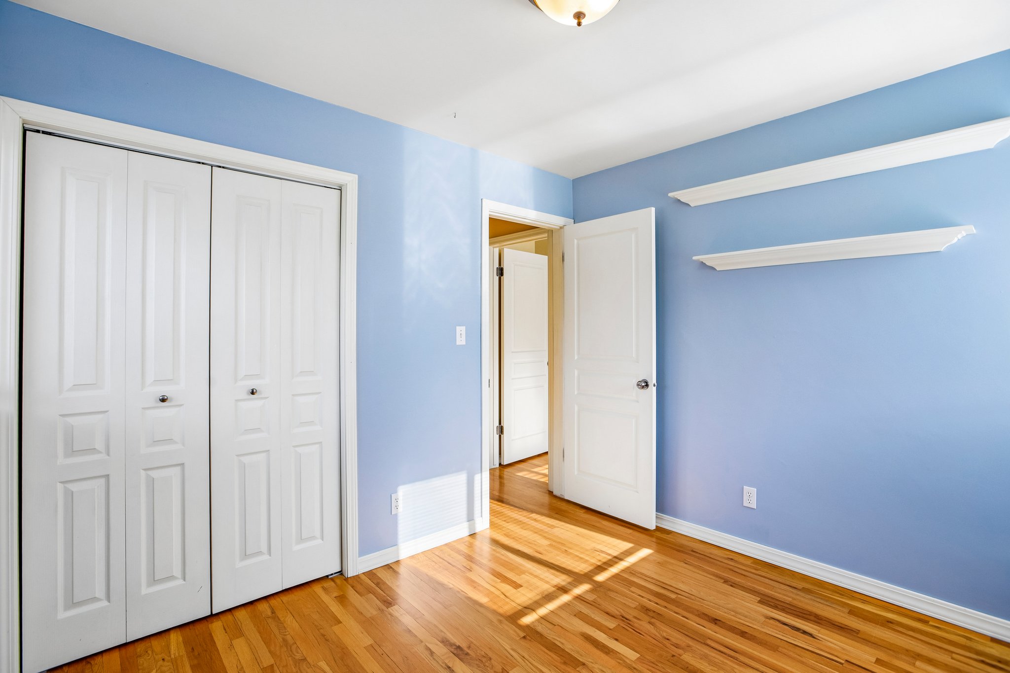 Hardwood flooring with bi-fold closet doors, white trim, and a ceiling-mounted light fixture