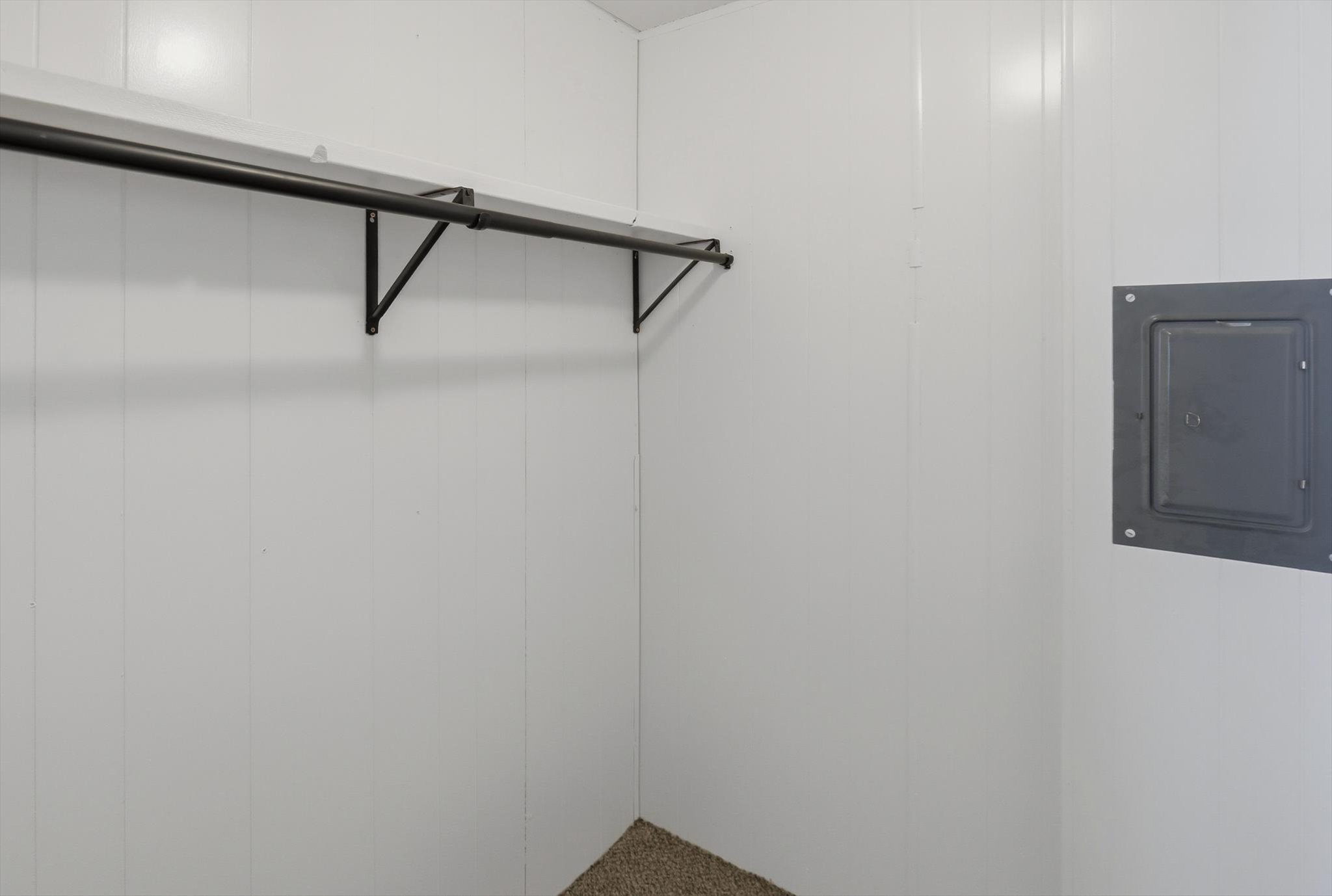 White paneled walls featuring a black metal clothing rod and a recessed utility panel