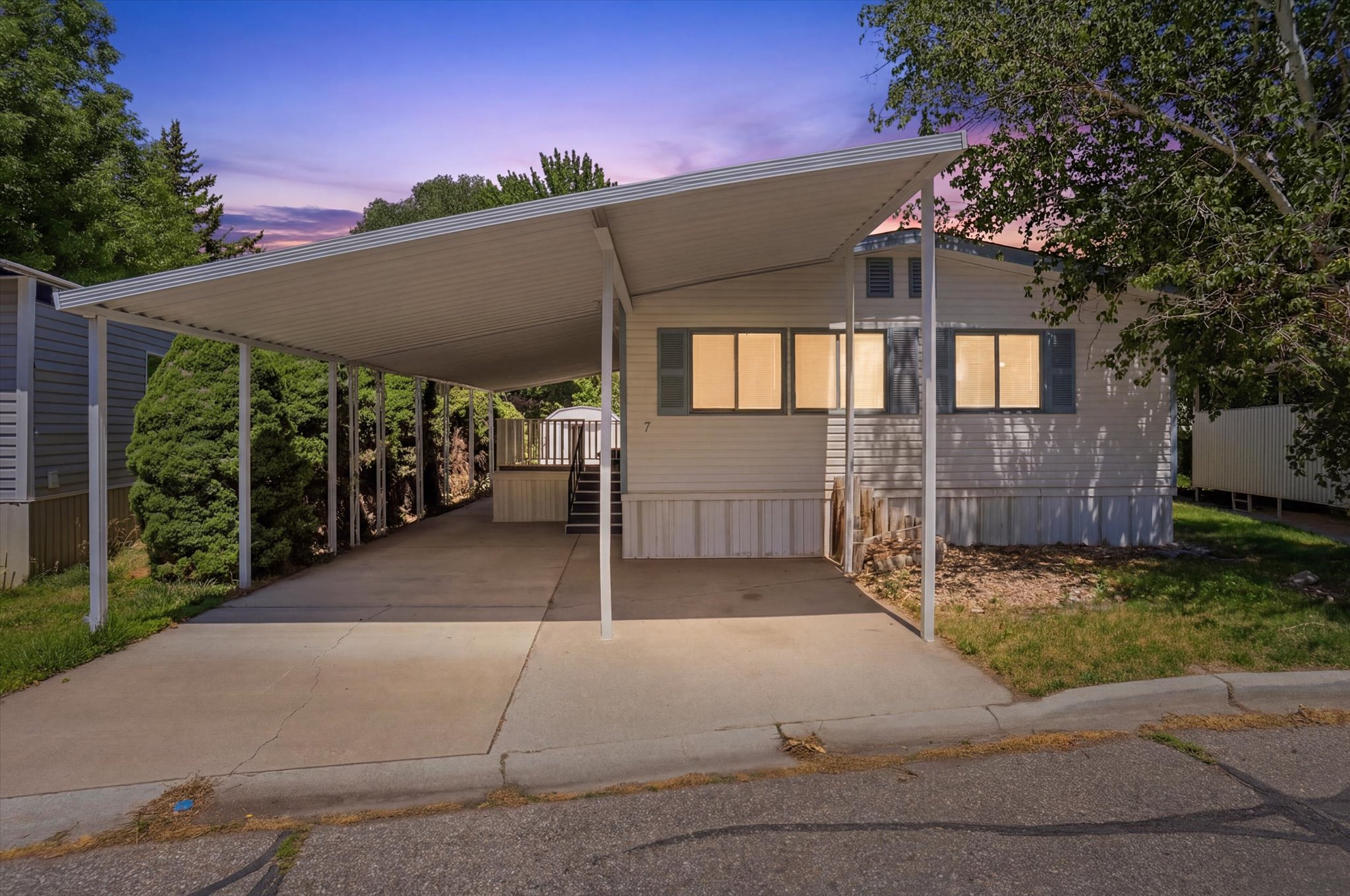 Exterior featuring white siding, a covered carport, and mature perimeter trees
