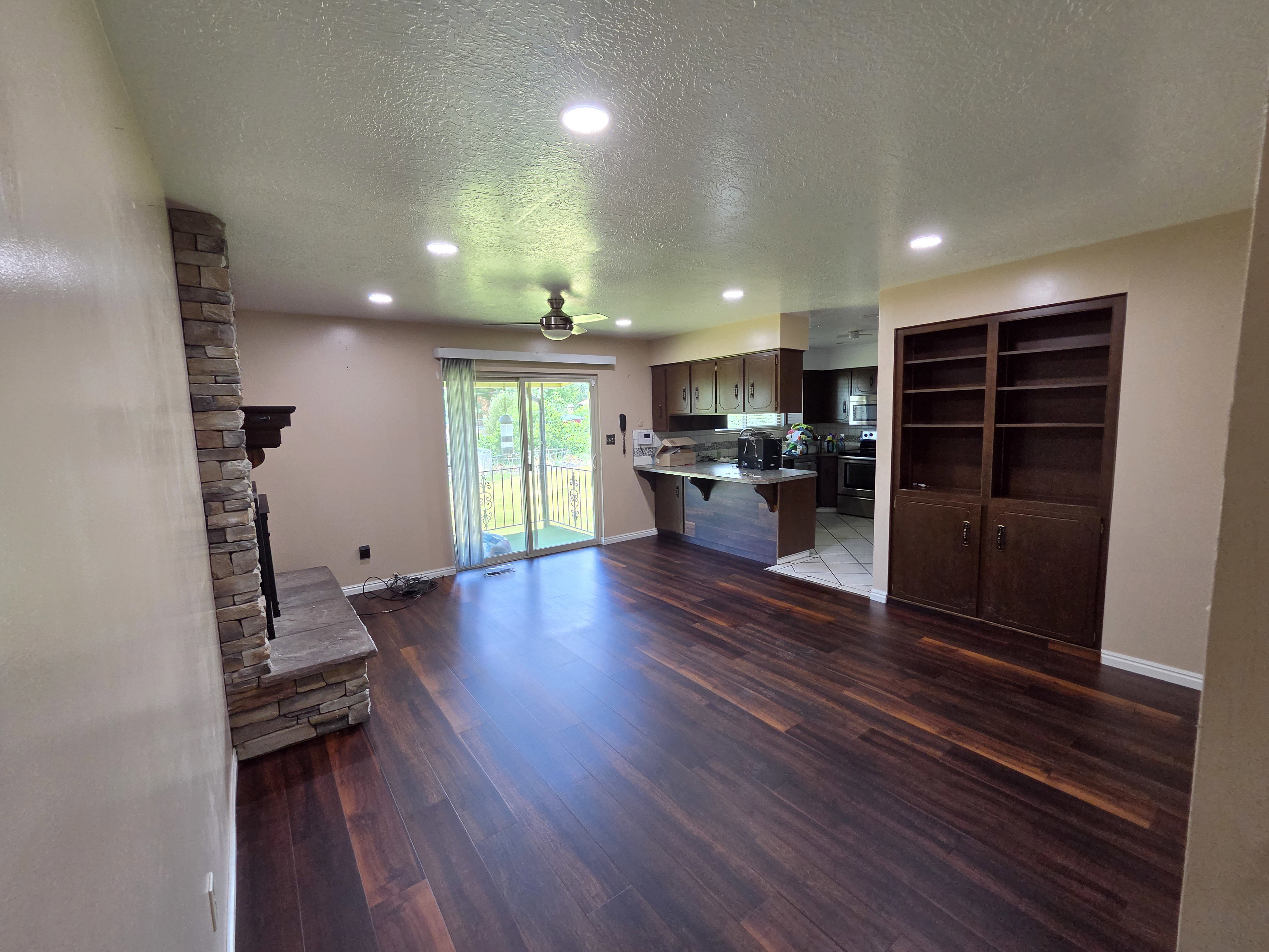 Open concept living area featuring dark wood-finish flooring, a stacked stone fireplace with mantle, recessed lighting, and a ceiling fan