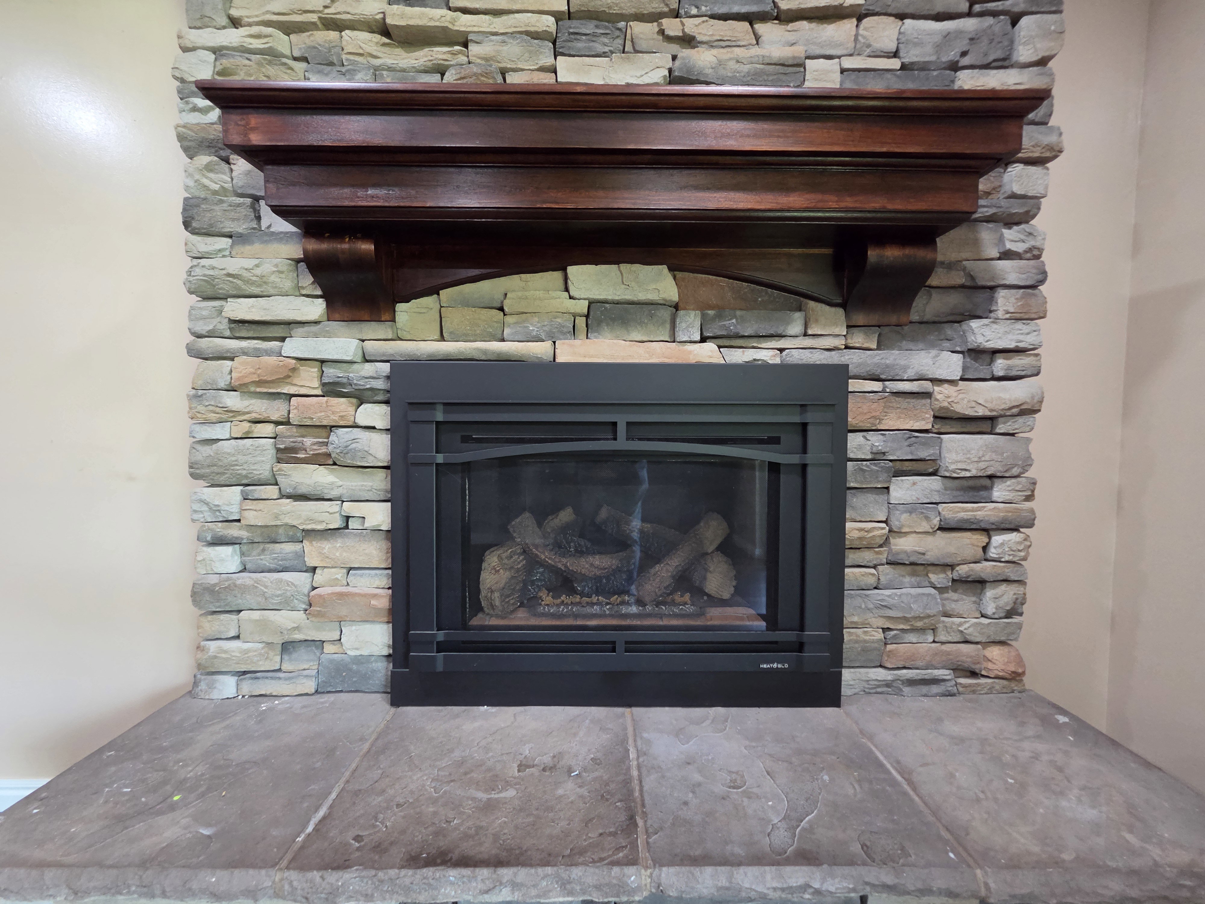 Stacked stone fireplace featuring a dark wood mantel and a large stone hearth