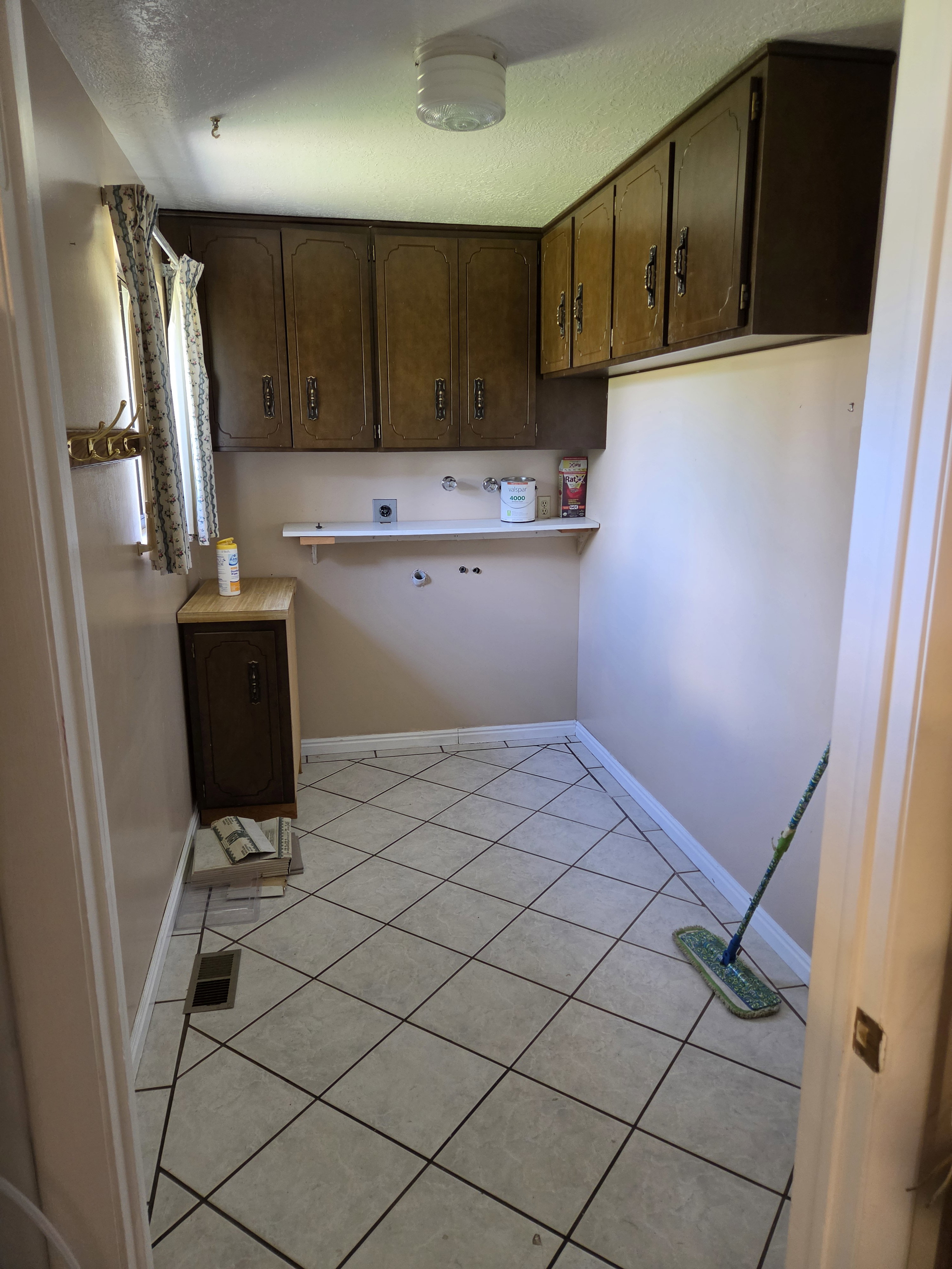 Utility room featuring extensive upper cabinetry, white tile flooring with dark grout, a wall-mounted shelving unit, and a single window