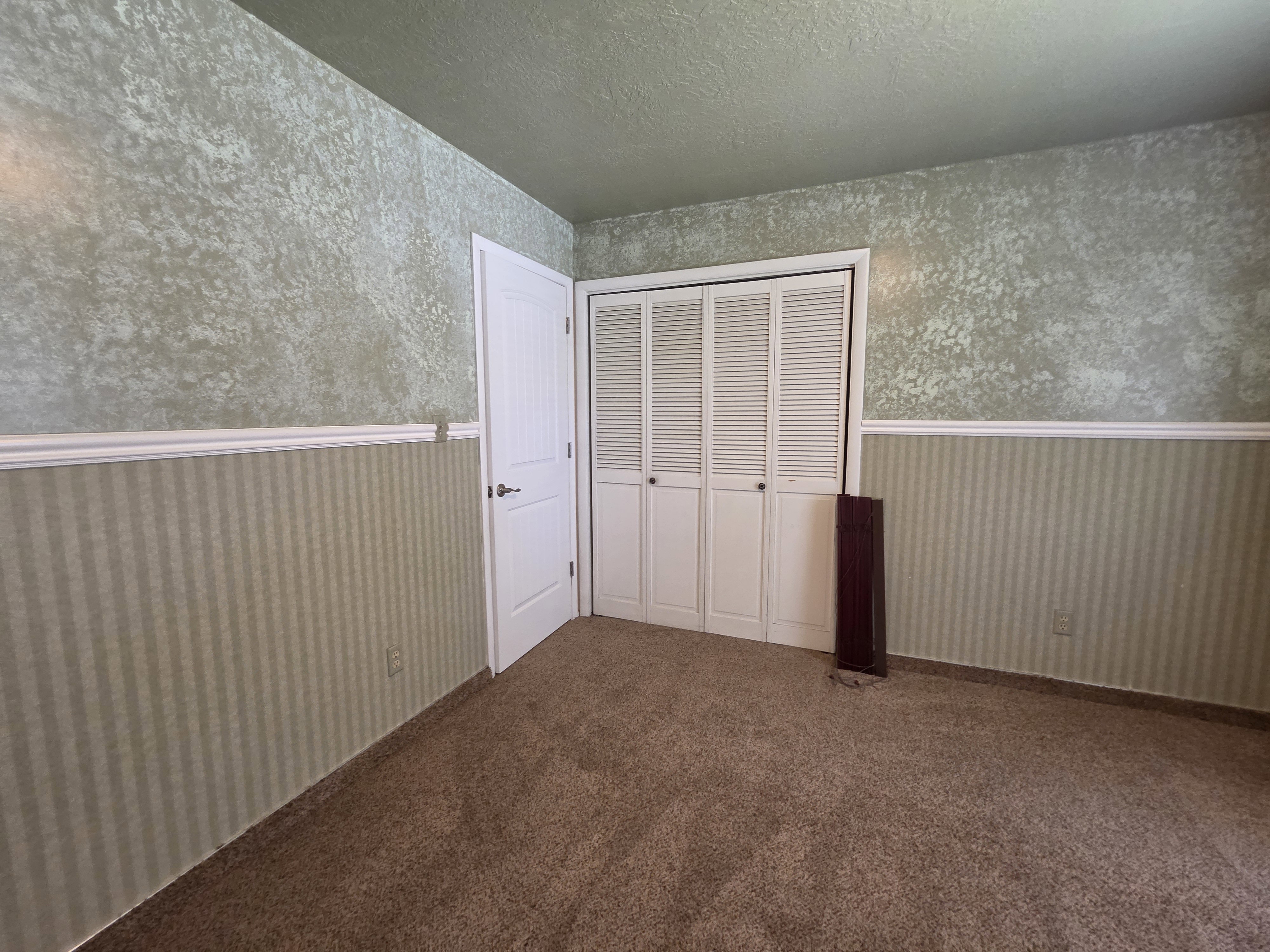 Carpeted room featuring a white paneled door, bi-fold closet doors, chair rail molding, and striped wall paneling