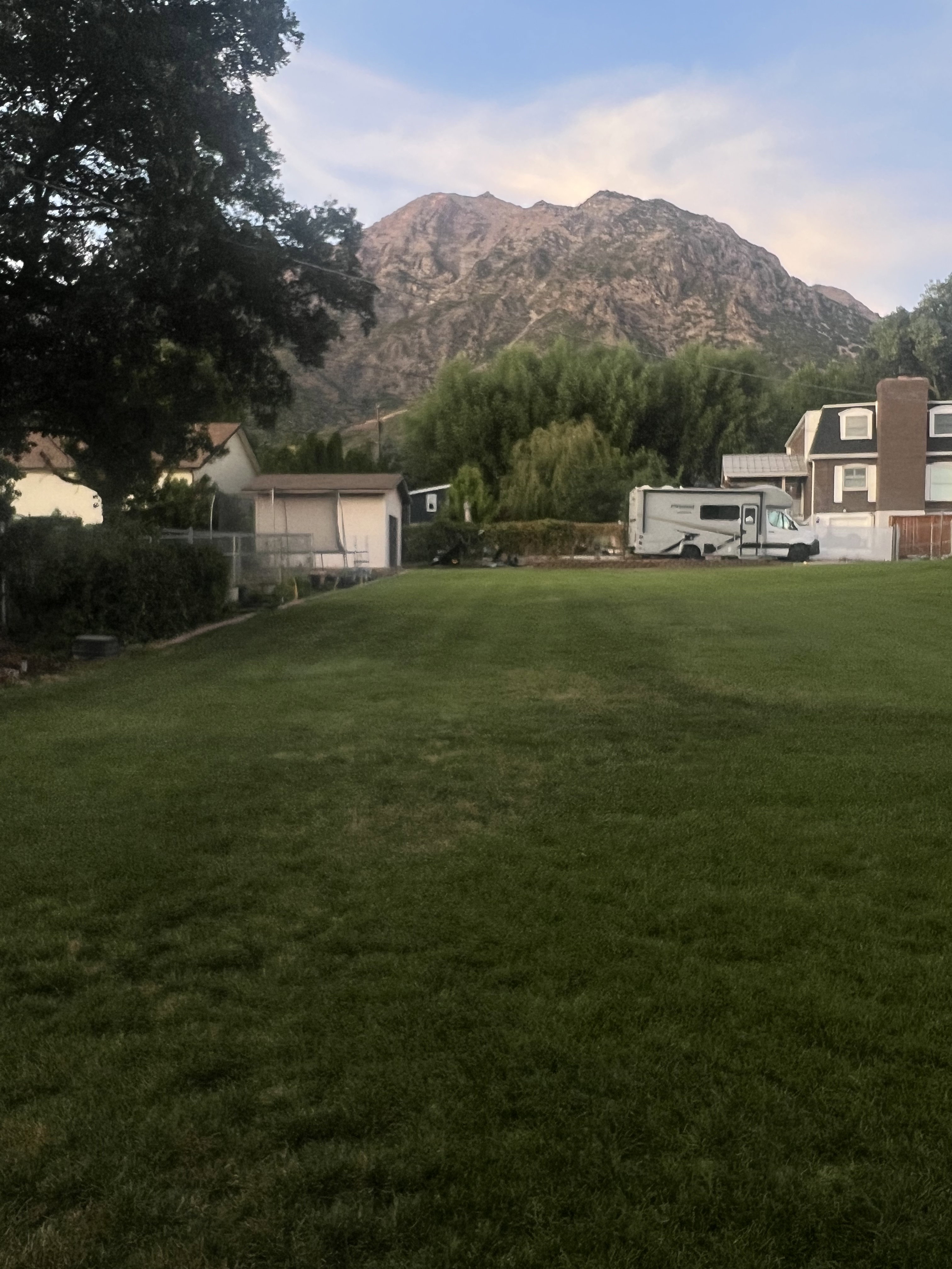 Expansive lawn with mature perimeter trees, a detached storage building, and a mountain backdrop