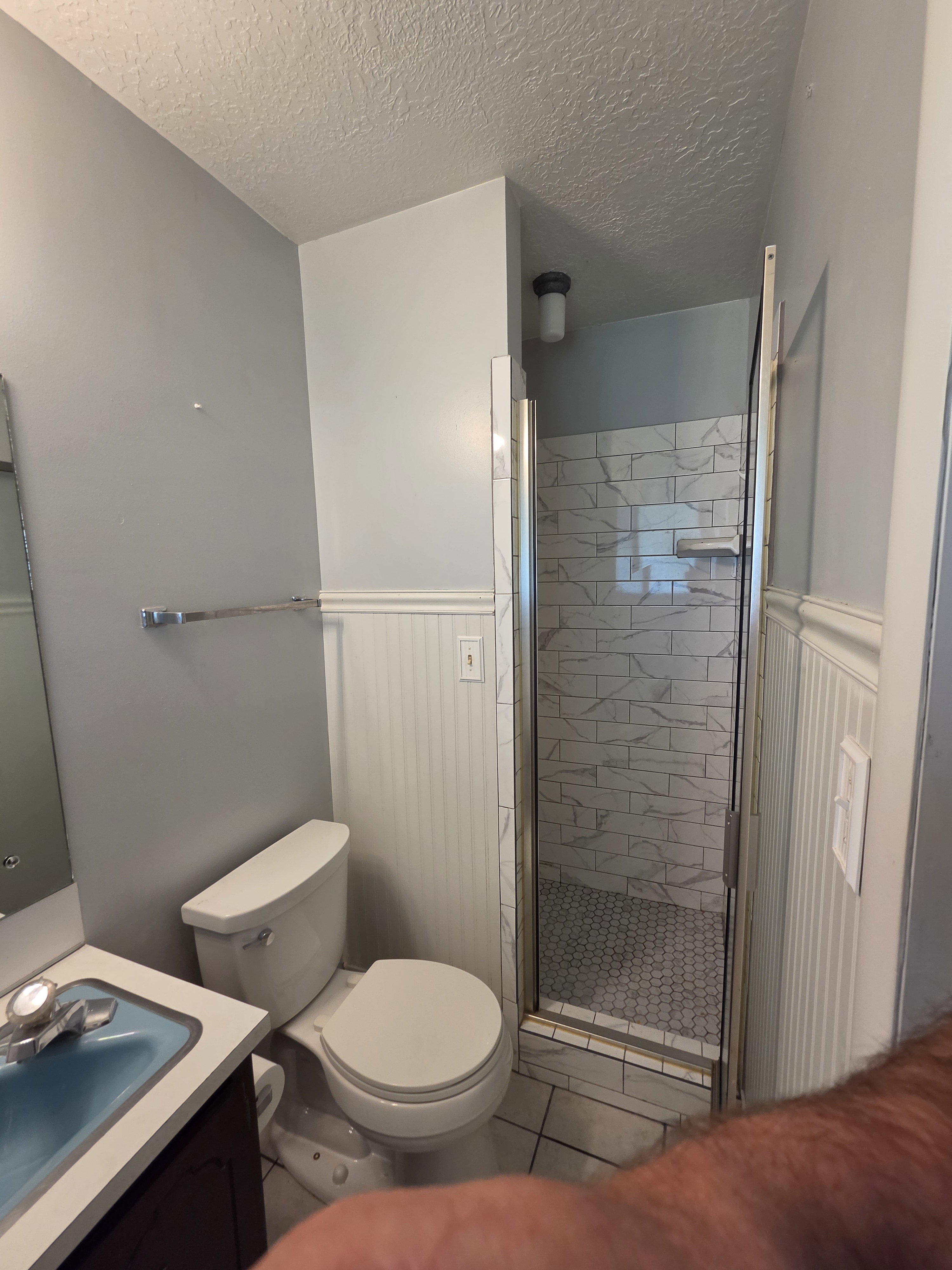 Compact bathroom featuring a shower with glass enclosure, white subway tile surround, and hexagonal floor tiles