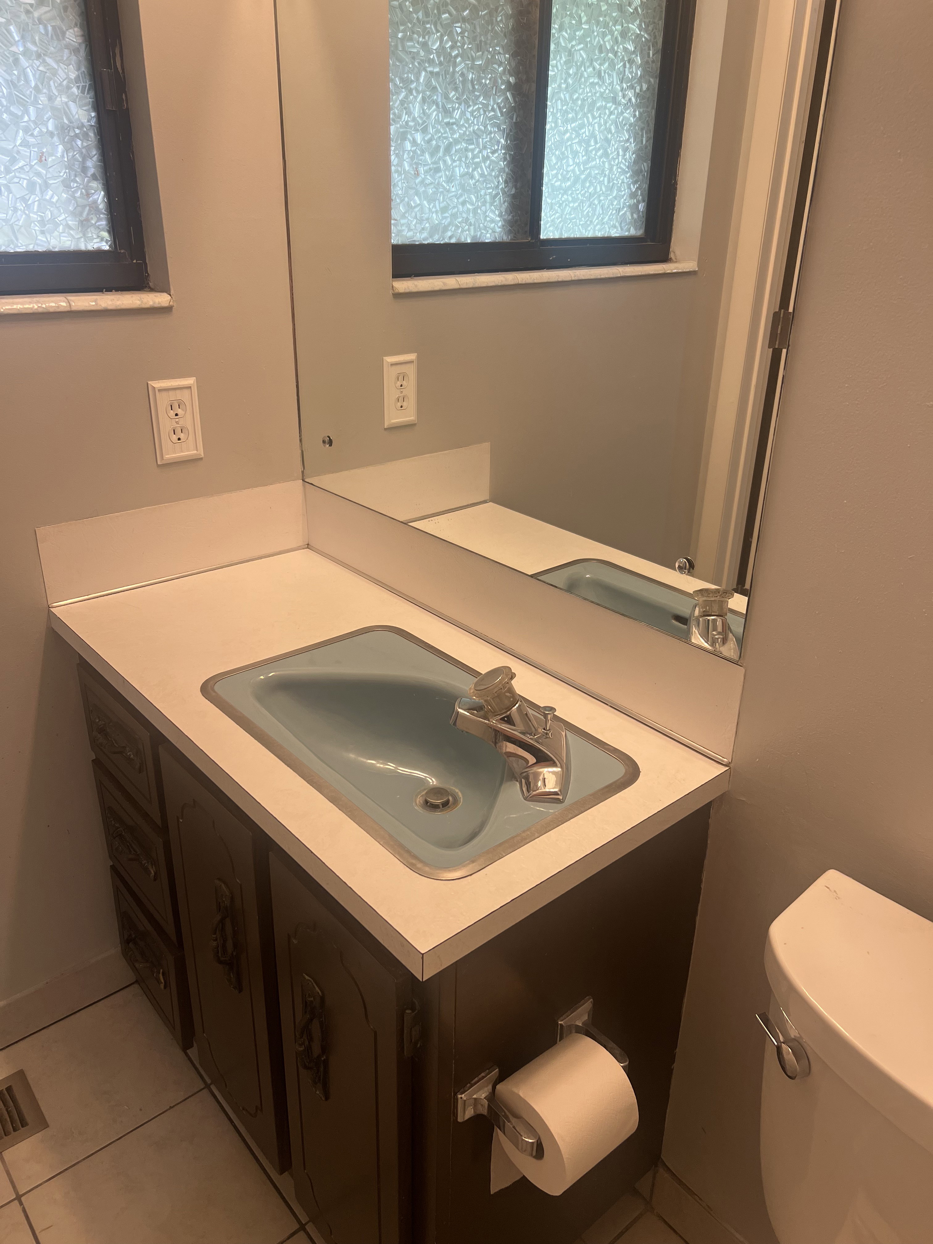 Bathroom vanity with a light blue drop-in sink, chrome faucet, and white laminate countertop