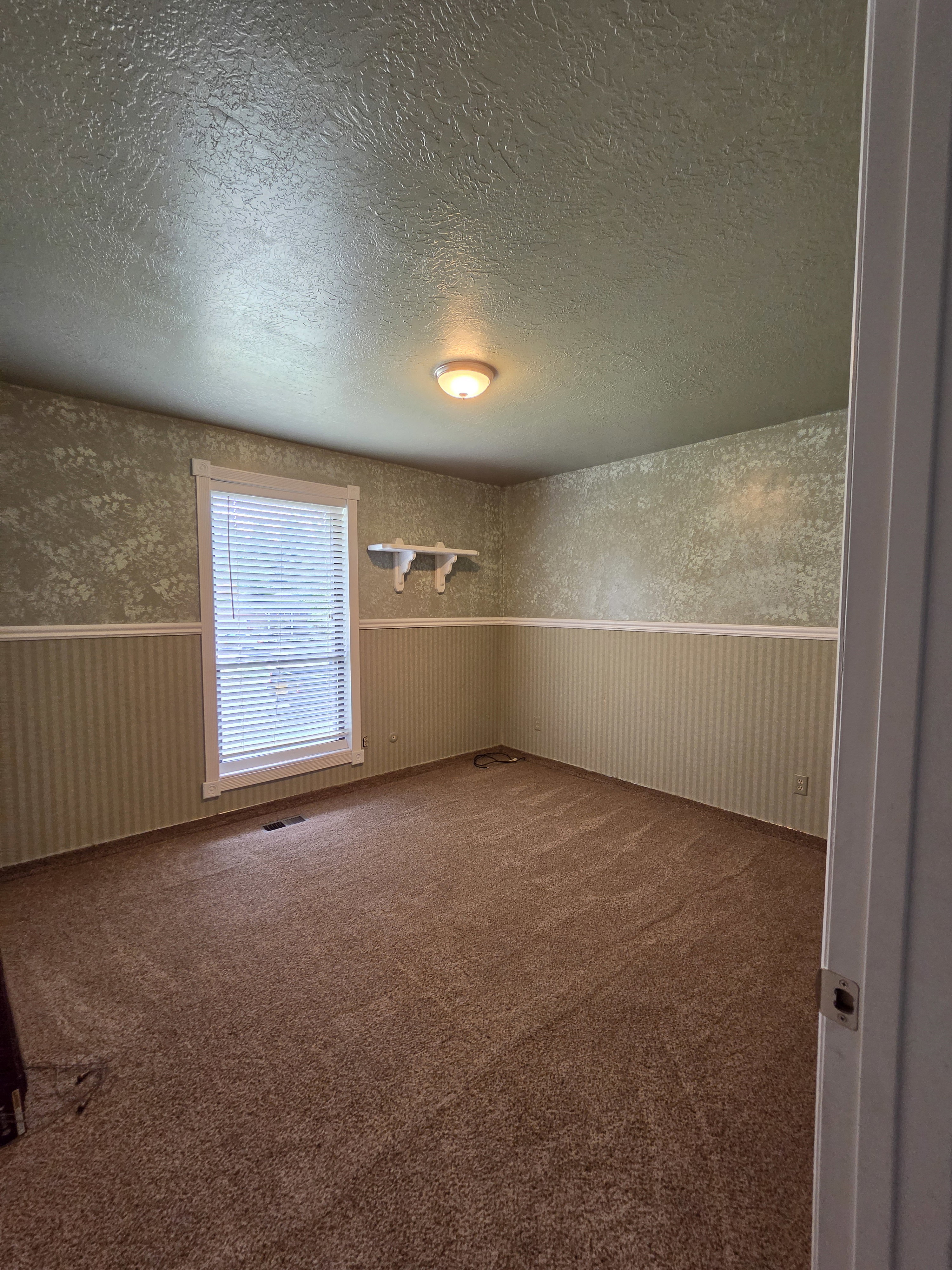 Spacious room featuring broadloom carpeting, a single window with blinds, and a built-in wall shelf