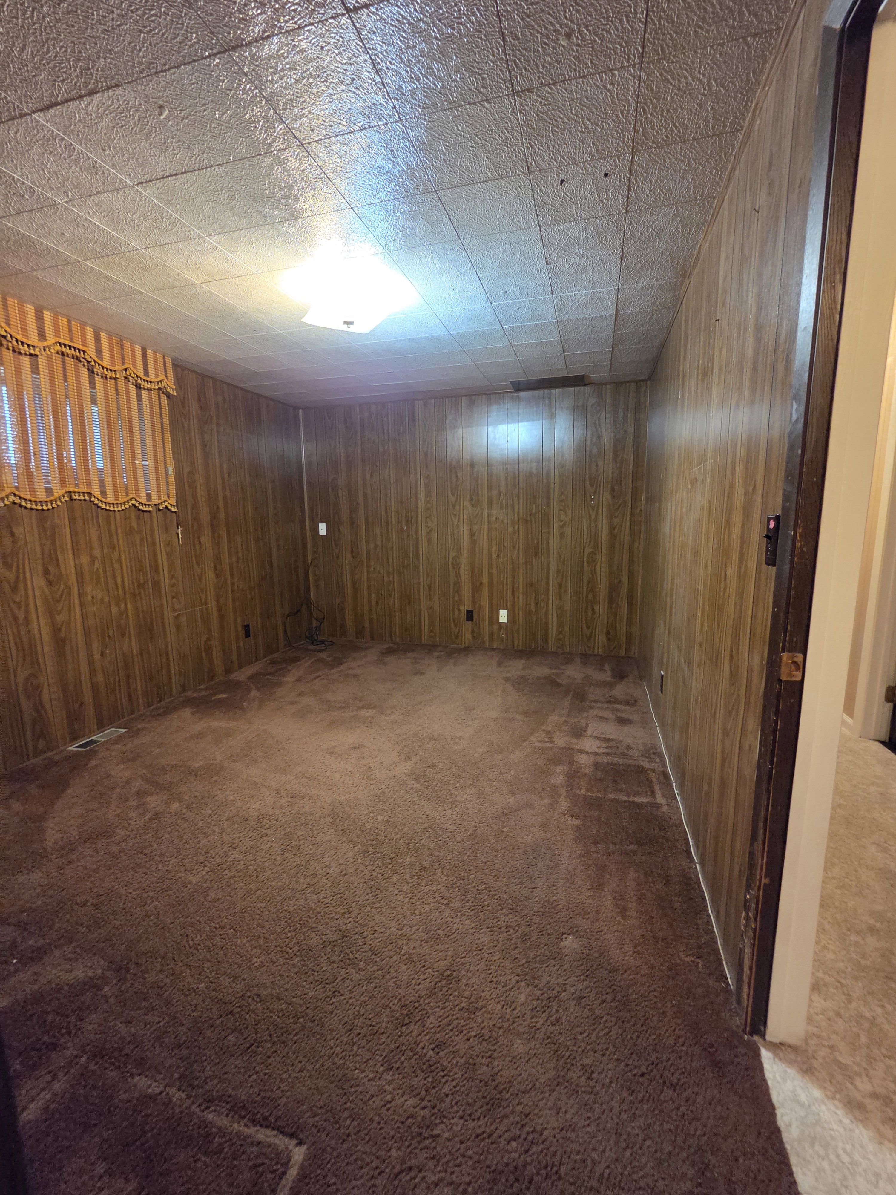 Carpeted room featuring wood-panel walls and a drop ceiling with recessed lighting