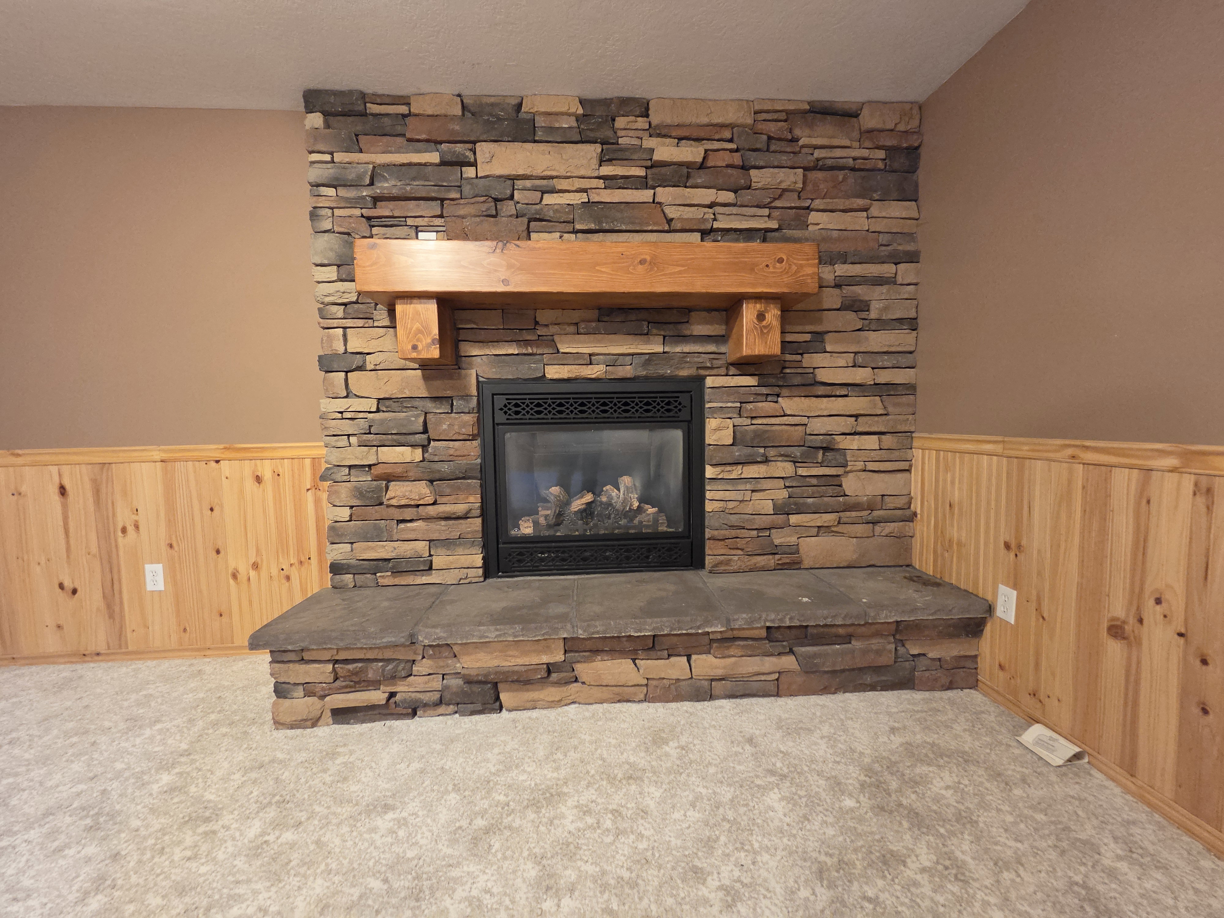 Stacked stone fireplace with a substantial wood mantel, a black metal firebox, and a stone hearth