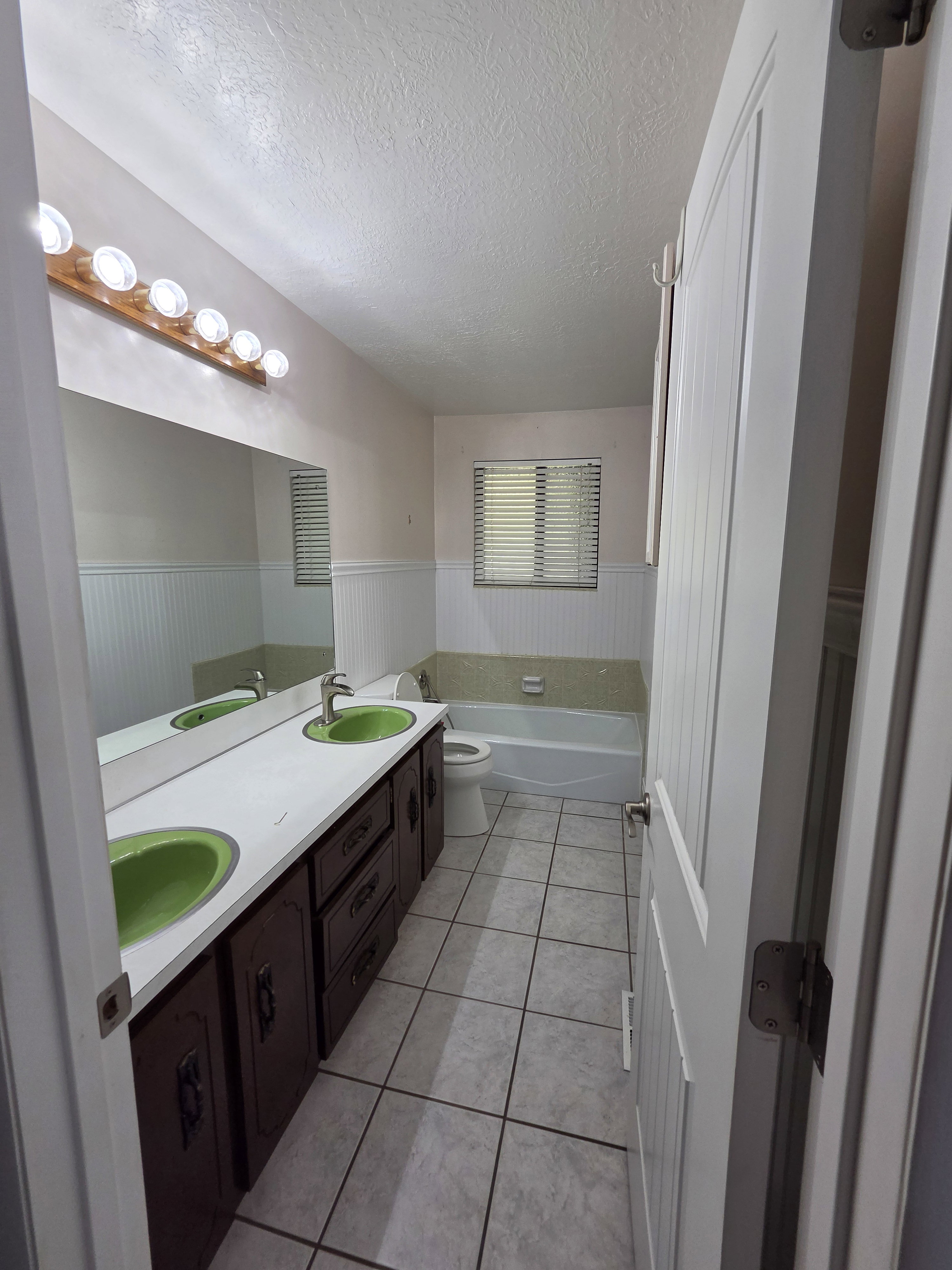 Bathroom featuring a dual vanity with green basin sinks, dark wood-finish cabinetry, and a full-width mirror