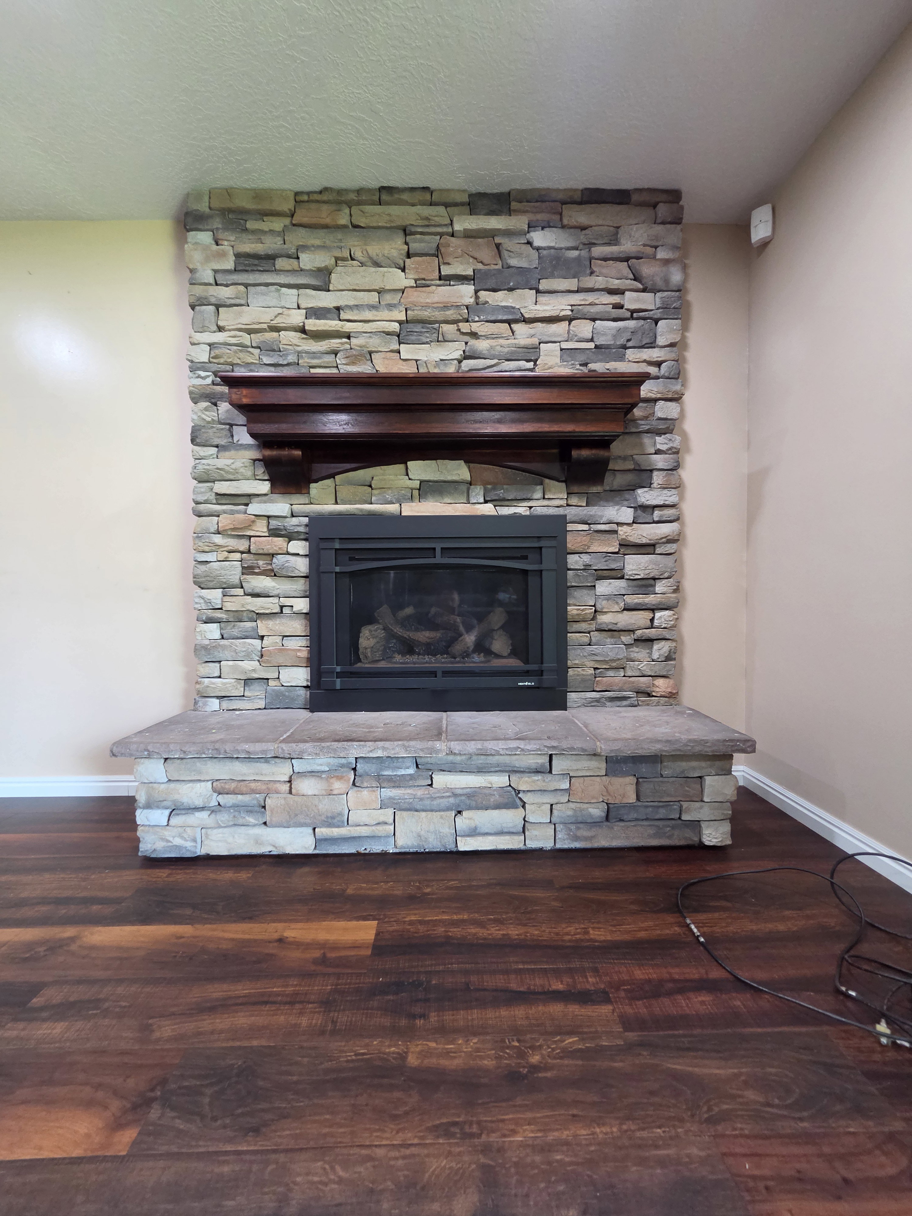 Stone-clad fireplace with a dark wood mantel and a gas insert