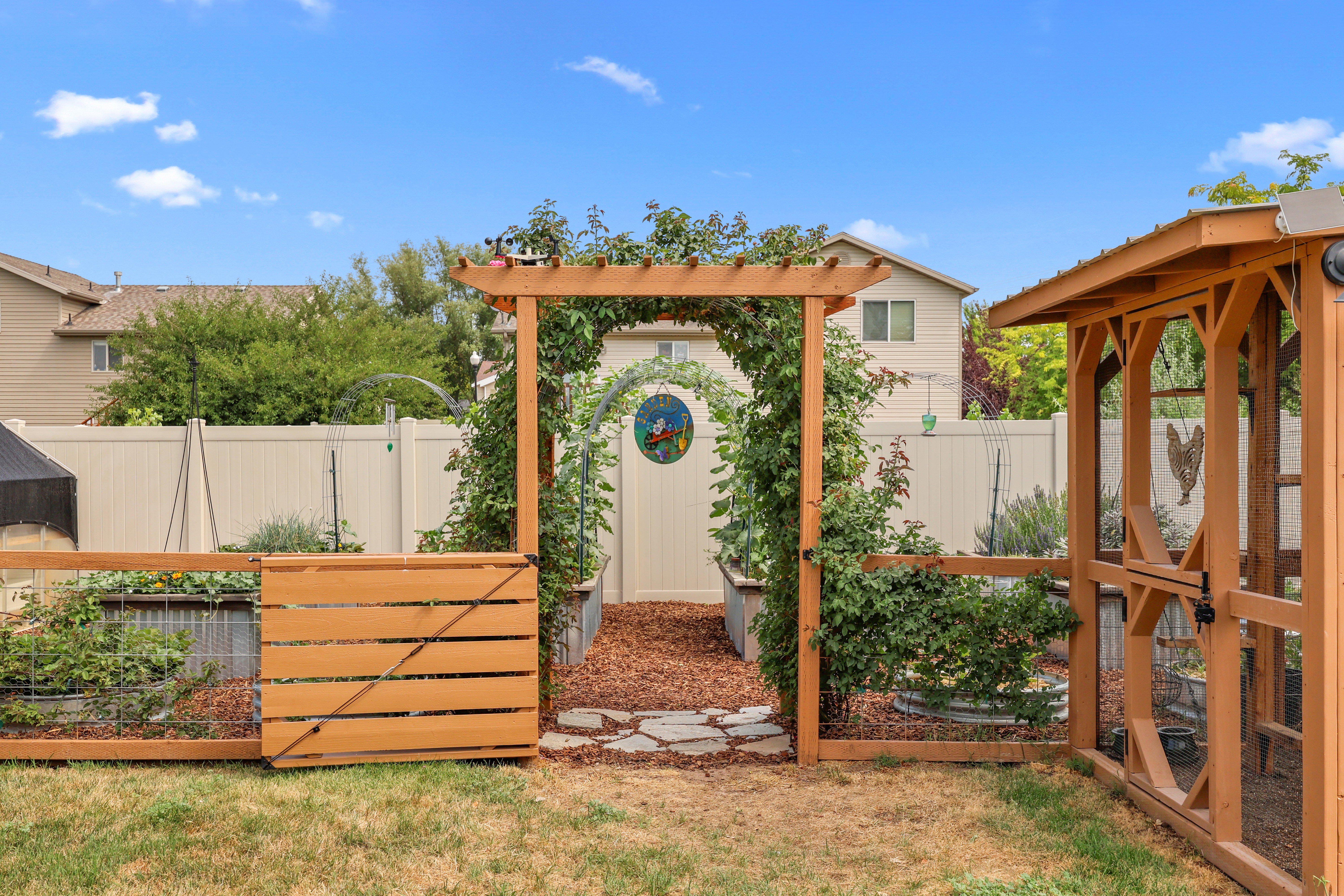 Backyard featuring a wooden pergola entrance into garden area with raised garden beds