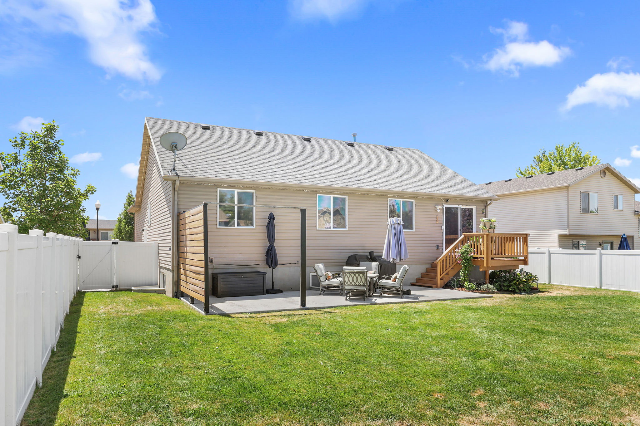 Spacious backyard featuring a manicured lawn, white vinyl fencing, a concrete patio, and a wood deck with stairs