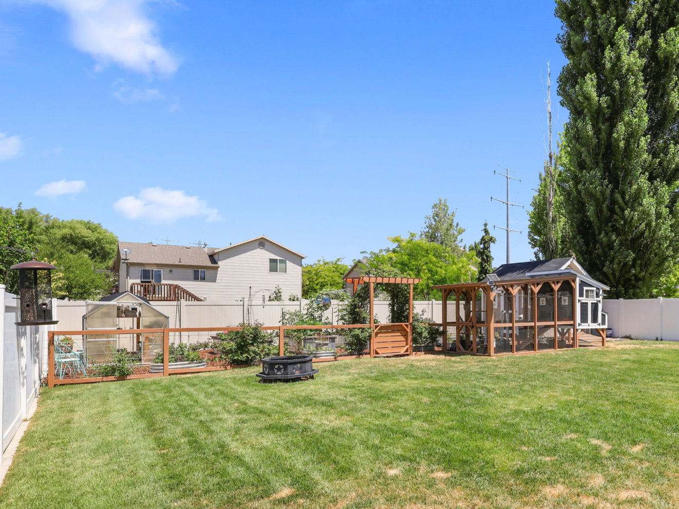 Expansive backyard featuring a large lawn, a white privacy fence, a dedicated gardening area with a greenhouse, and an additional outdoor structure
