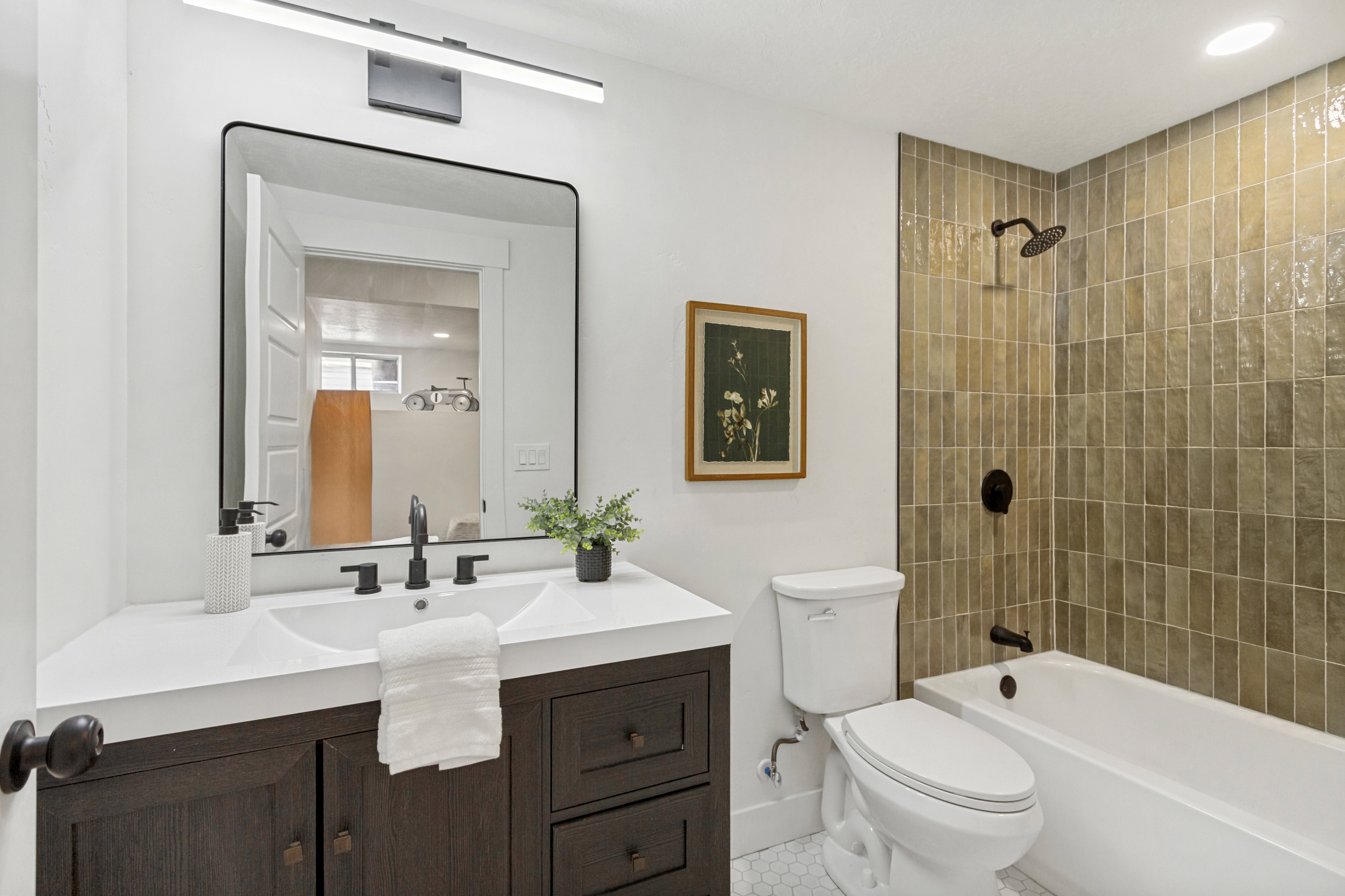 Contemporary bathroom featuring a dark wood-finish vanity with an integrated dual sink countertop, a large framed mirror, and matte black fixtures