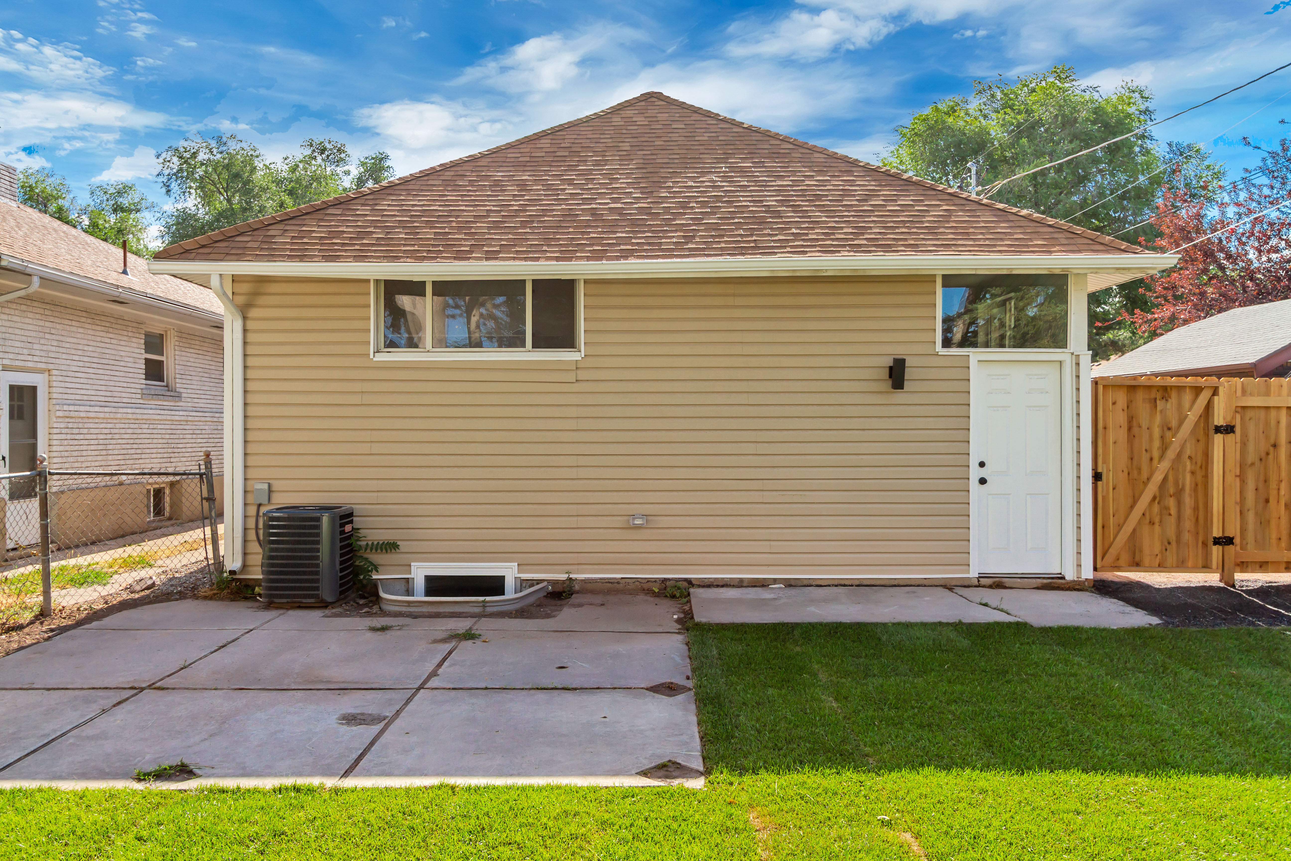 Rear exterior featuring beige siding, a brown shingle roof, and a concrete patio