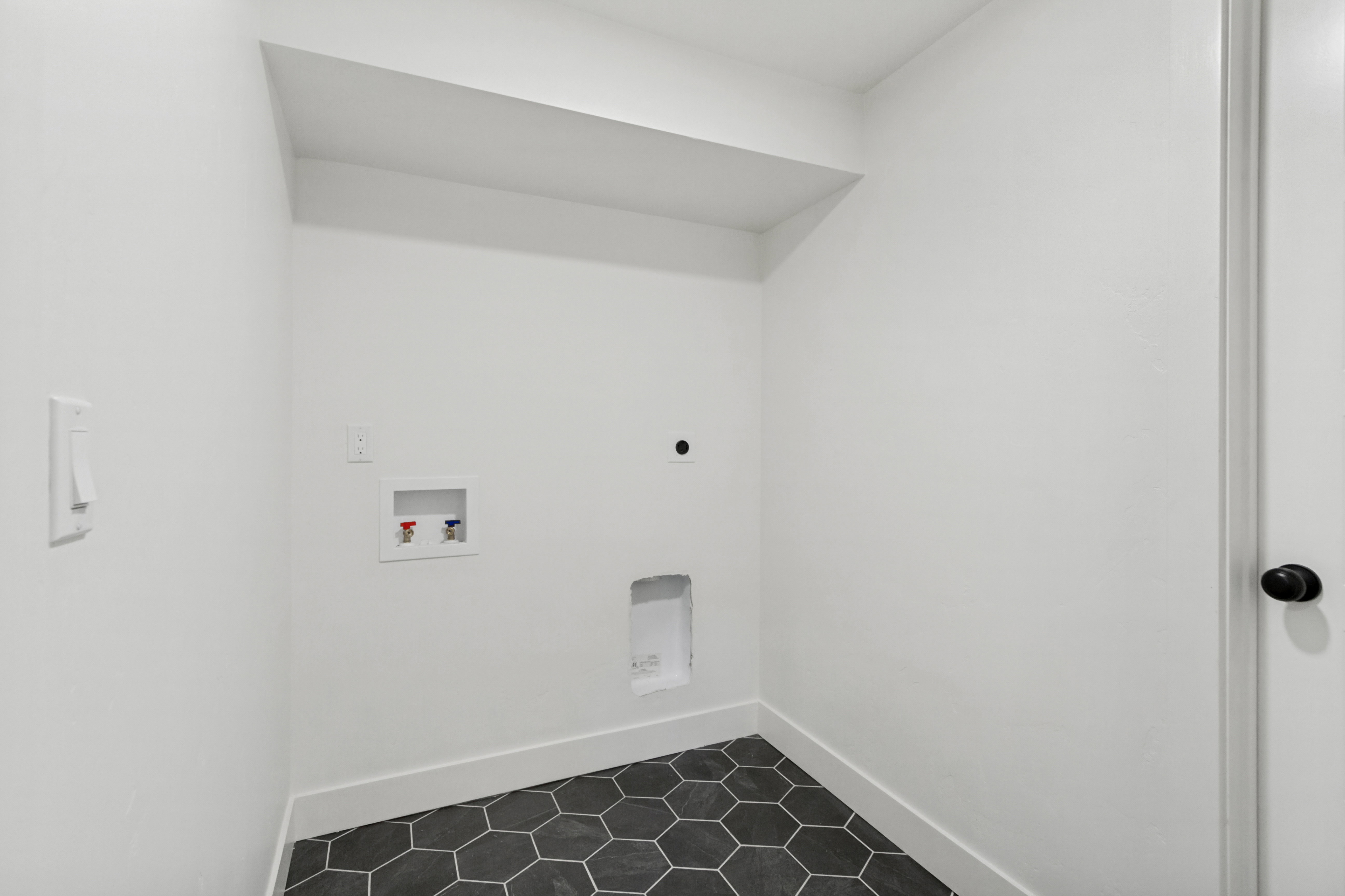 Dedicated laundry area featuring a white color palette, dark hexagonal floor tiles, and a white baseboard trim