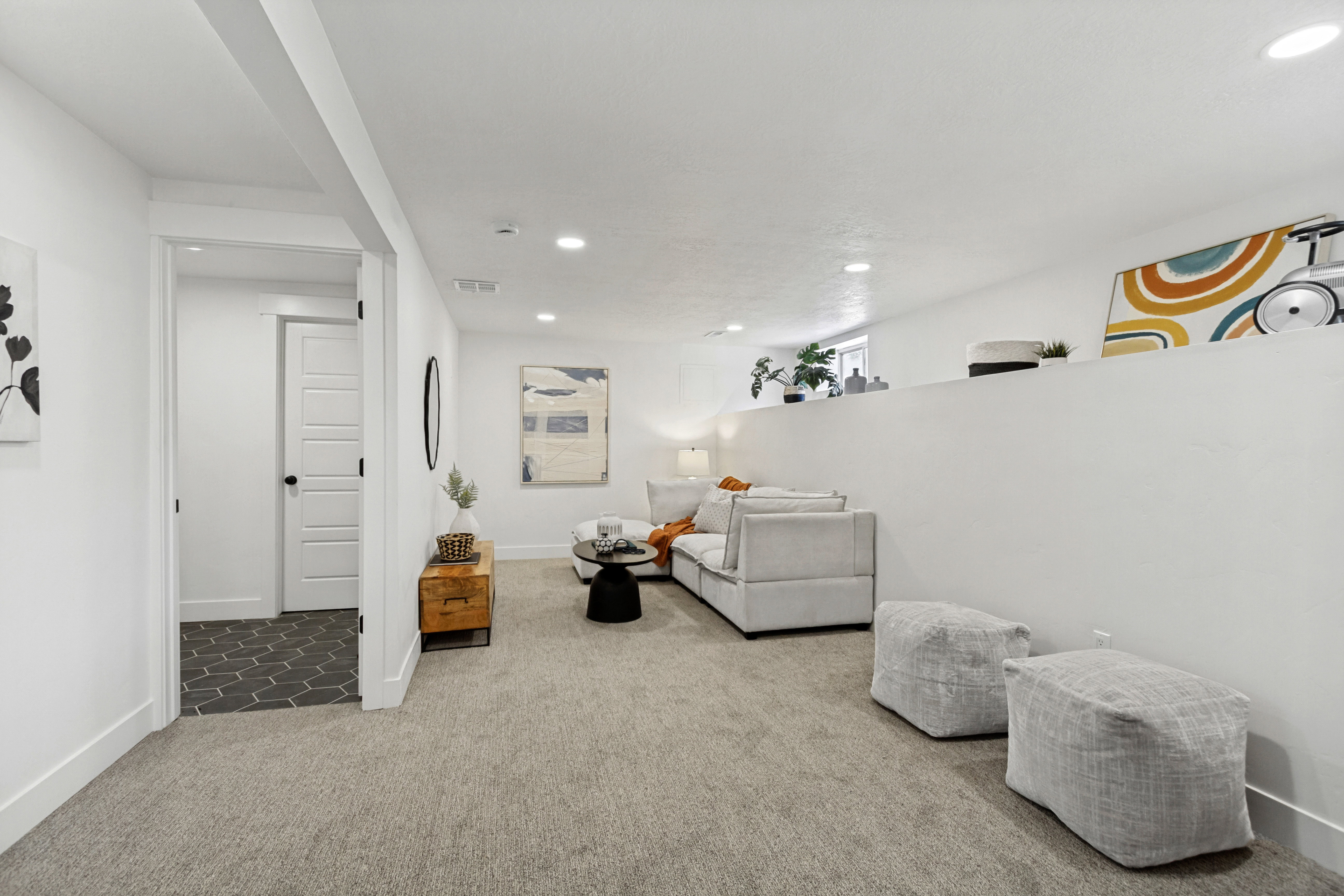 Carpeted recreation area with recessed lighting, a half-wall partition, and a doorway opening to a dark hexagonal tile floor