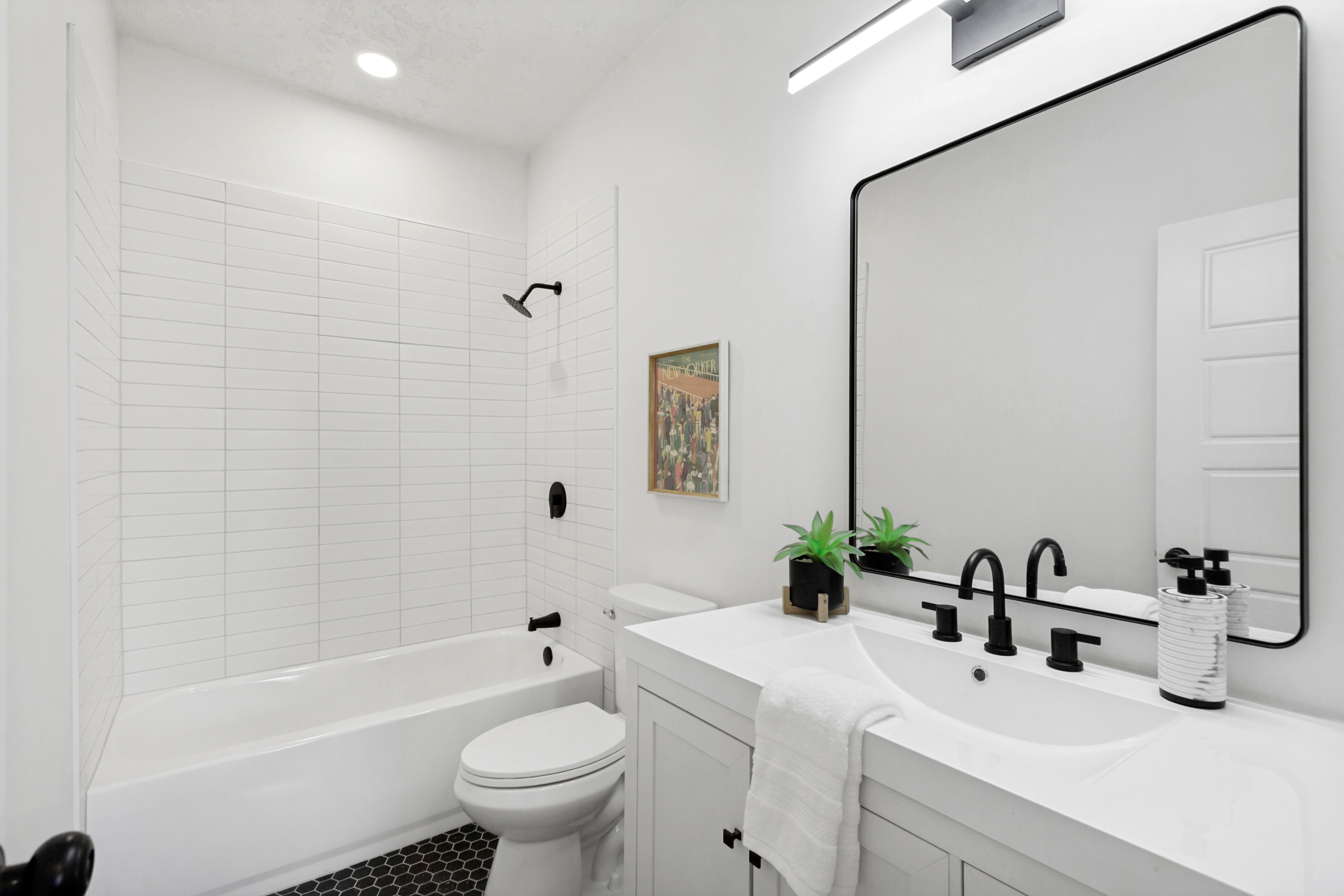 Bathroom featuring a single vanity with an integrated sink, matte black fixtures, a rectangular framed mirror, and a full bathtub with white subway tile surround
