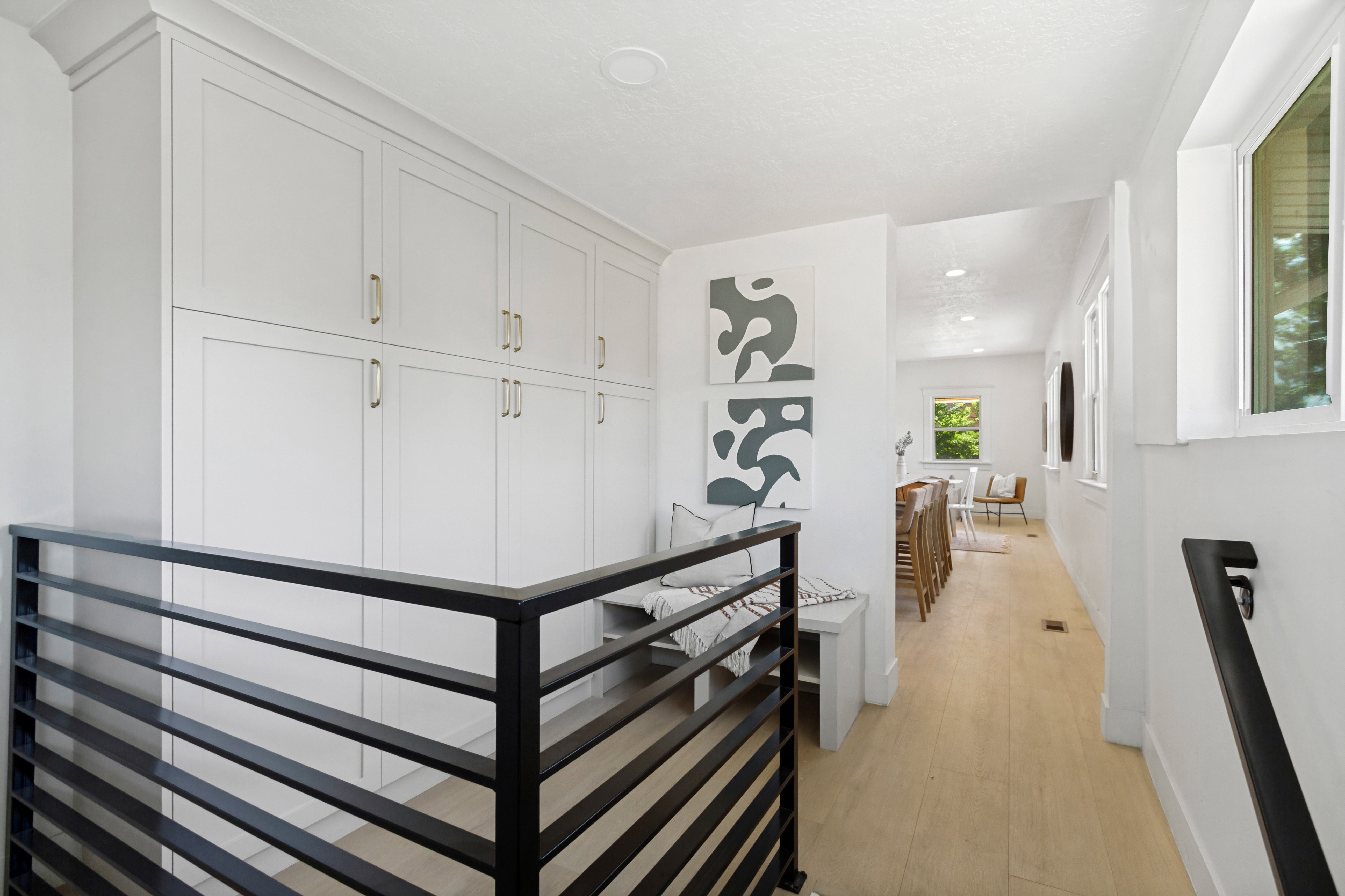 Hallway featuring extensive built-in cabinetry with gold-tone hardware, wood-finish flooring, and a modern horizontal slat railing