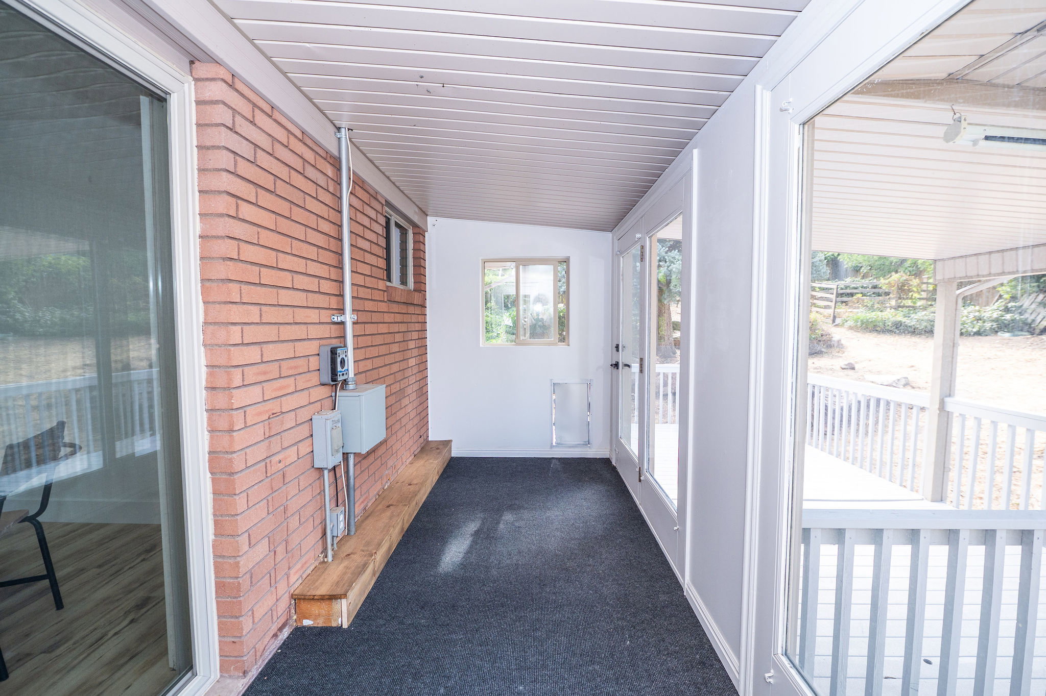Enclosed patio featuring a brick accent wall, white paneling, and a wood-finish bench