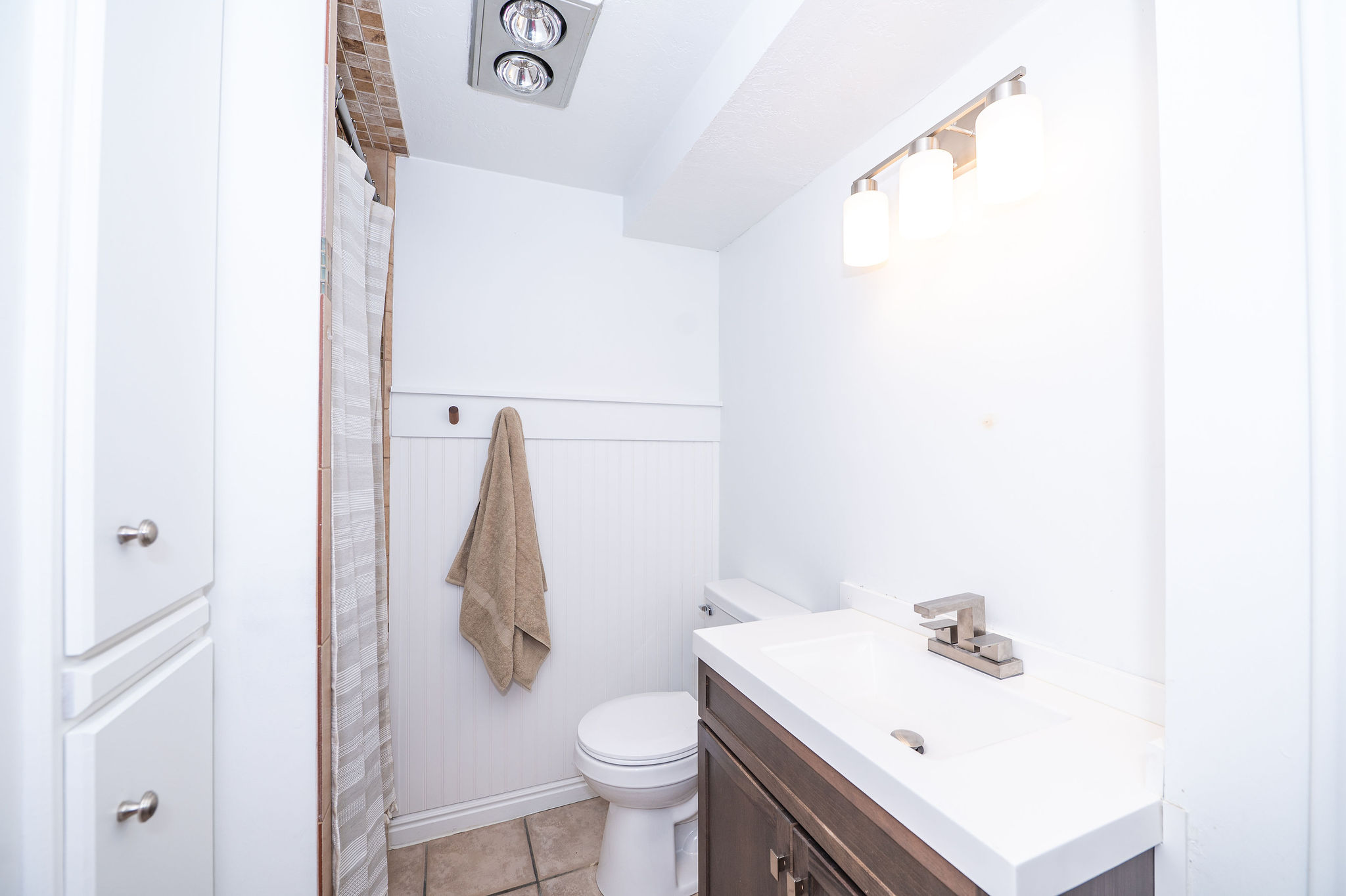 Bathroom featuring a dark wood-finish vanity with an integrated white sink, brushed nickel faucet, and a three-light vanity fixture