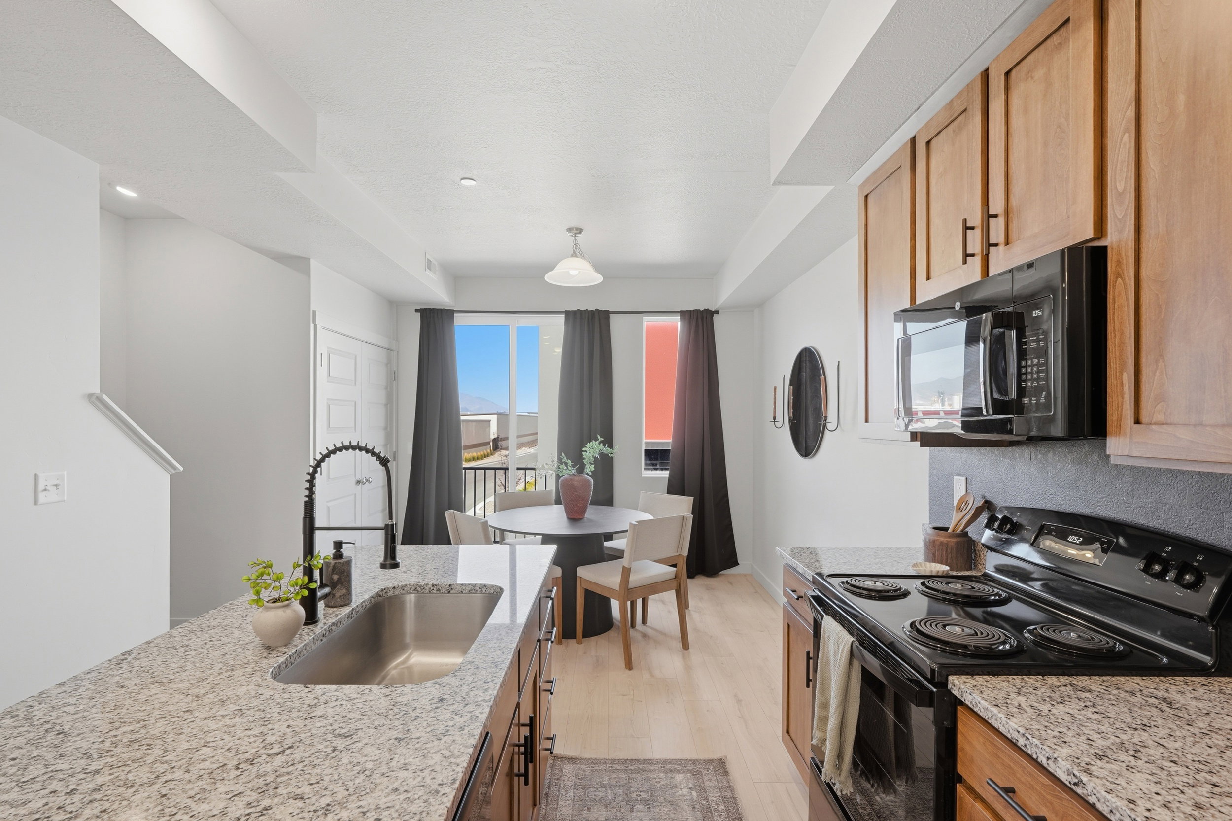Modern kitchen featuring granite countertops, wood cabinetry, a stainless steel undermount sink with a gooseneck faucet, and integrated black appliances
