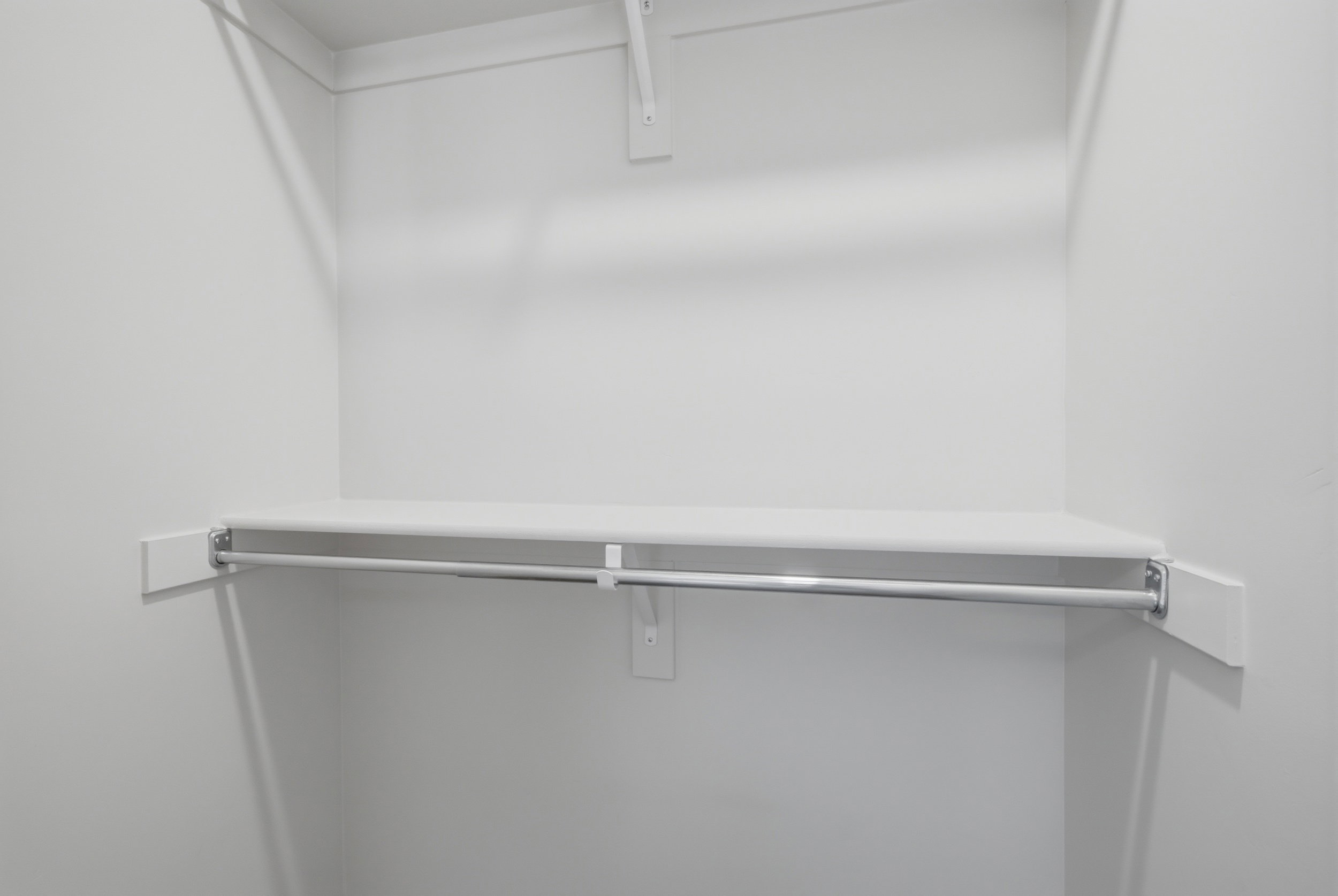 White-painted closet featuring a built-in shelf and chrome hanging rod