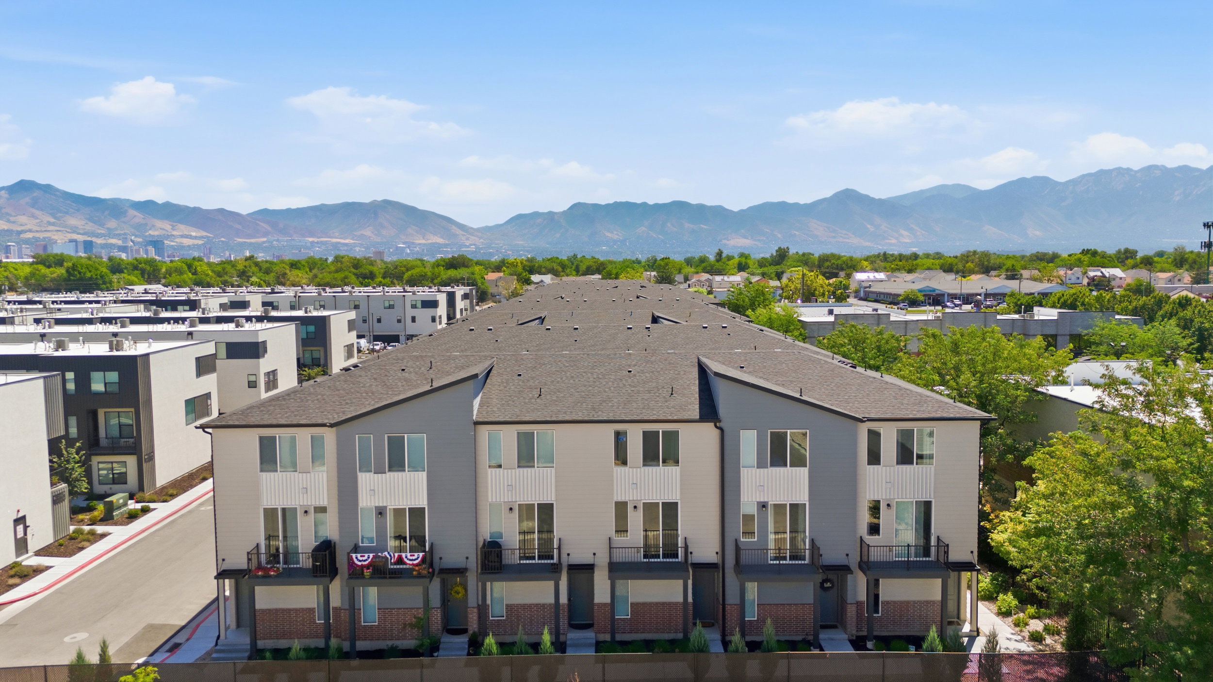 Modern townhome-style residences featuring gray and white siding, individual balconies with black railings, and brick accents on the lower level