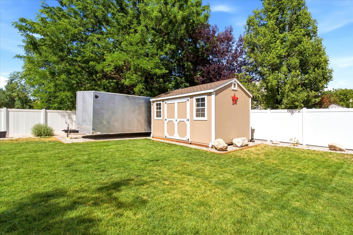 Expansive green lawn with a white privacy fence, Storage shed, and gravel parking area.