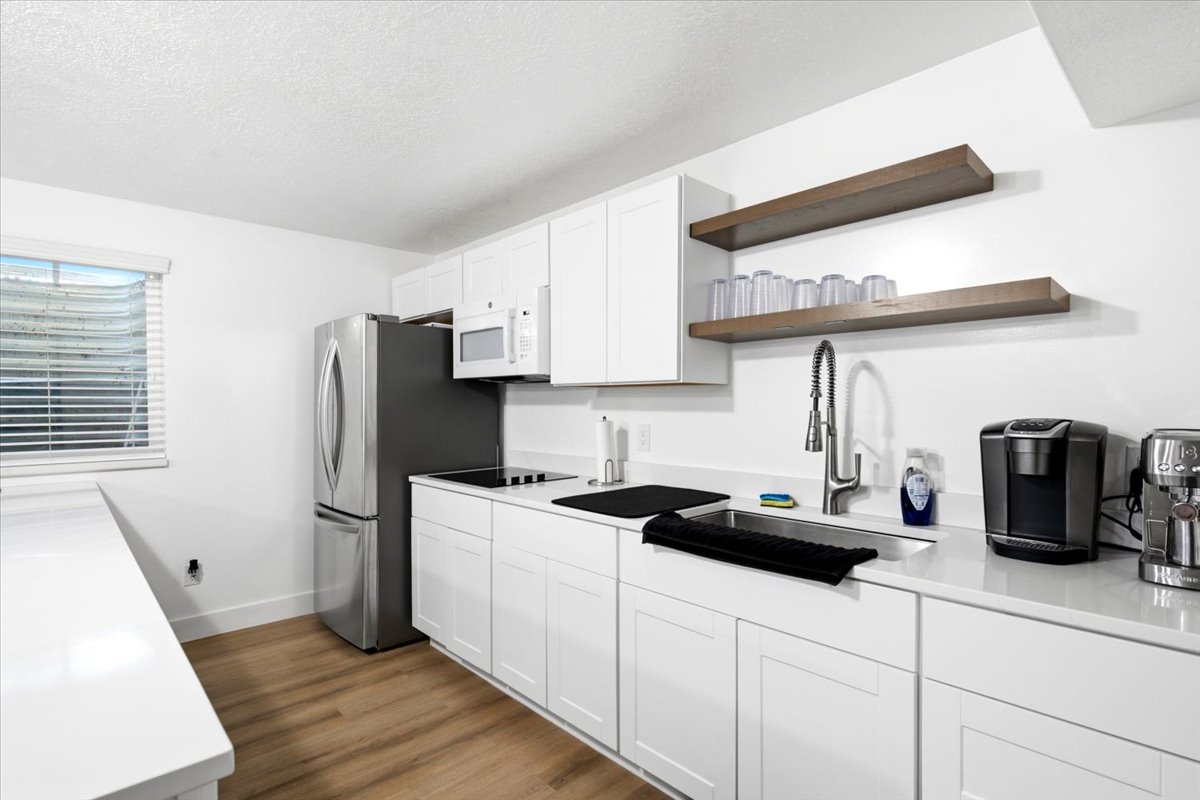 Modern kitchen featuring white cabinetry, light quarts countertops, wood-finish flooring, stainless steel appliances, and open wood shelving