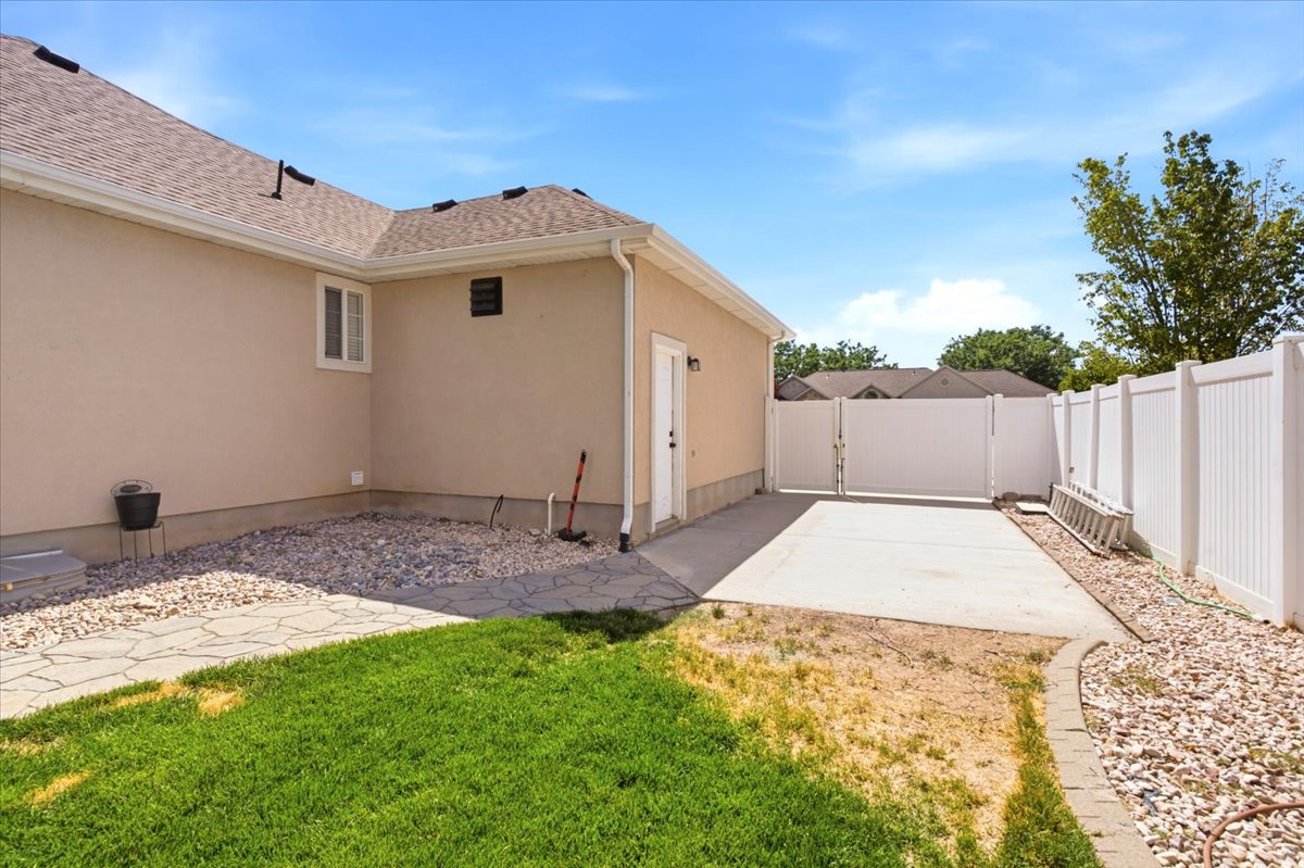Backyard space featuring a stucco exterior, concrete RV parking, white vinyl fencing, and a gravel area