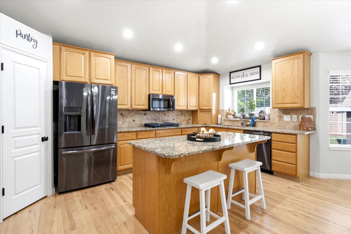 Kitchen featuring a central island with granite countertop, light wood-finish cabinetry, stainless steel appliances, and wood-finish flooring