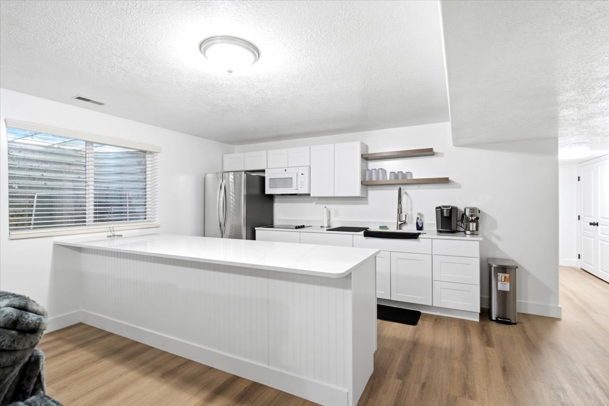 Modern second kitchen space featuring white cabinetry, stainless steel appliances, and a central island with a white quarts countertop