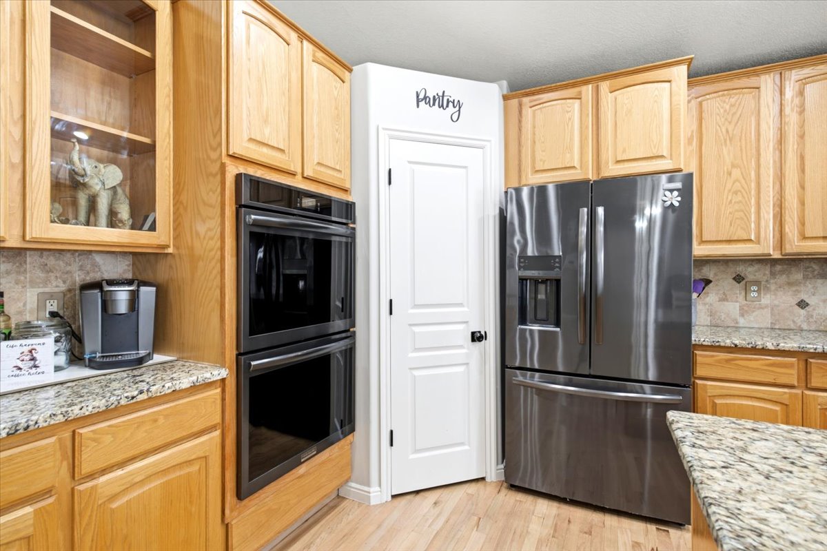 Kitchen featuring light wood cabinetry, stainless steel appliances, granite countertops, a tile backsplash, and a pantry
